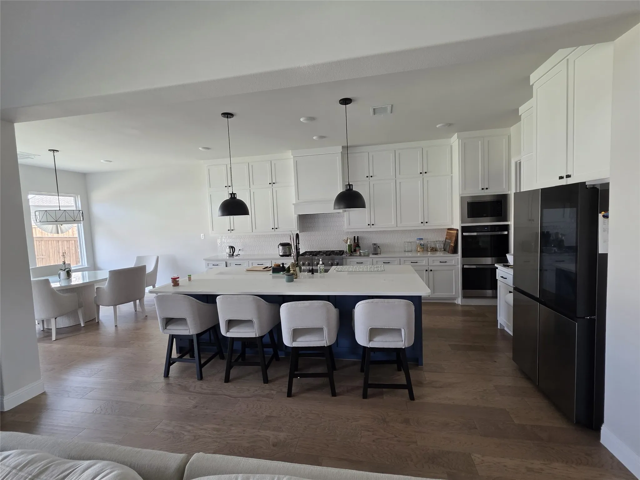 Kitchen featuring a central island, white shaker-style cabinetry, stainless steel appliances, wood-finish flooring, and pendant lighting