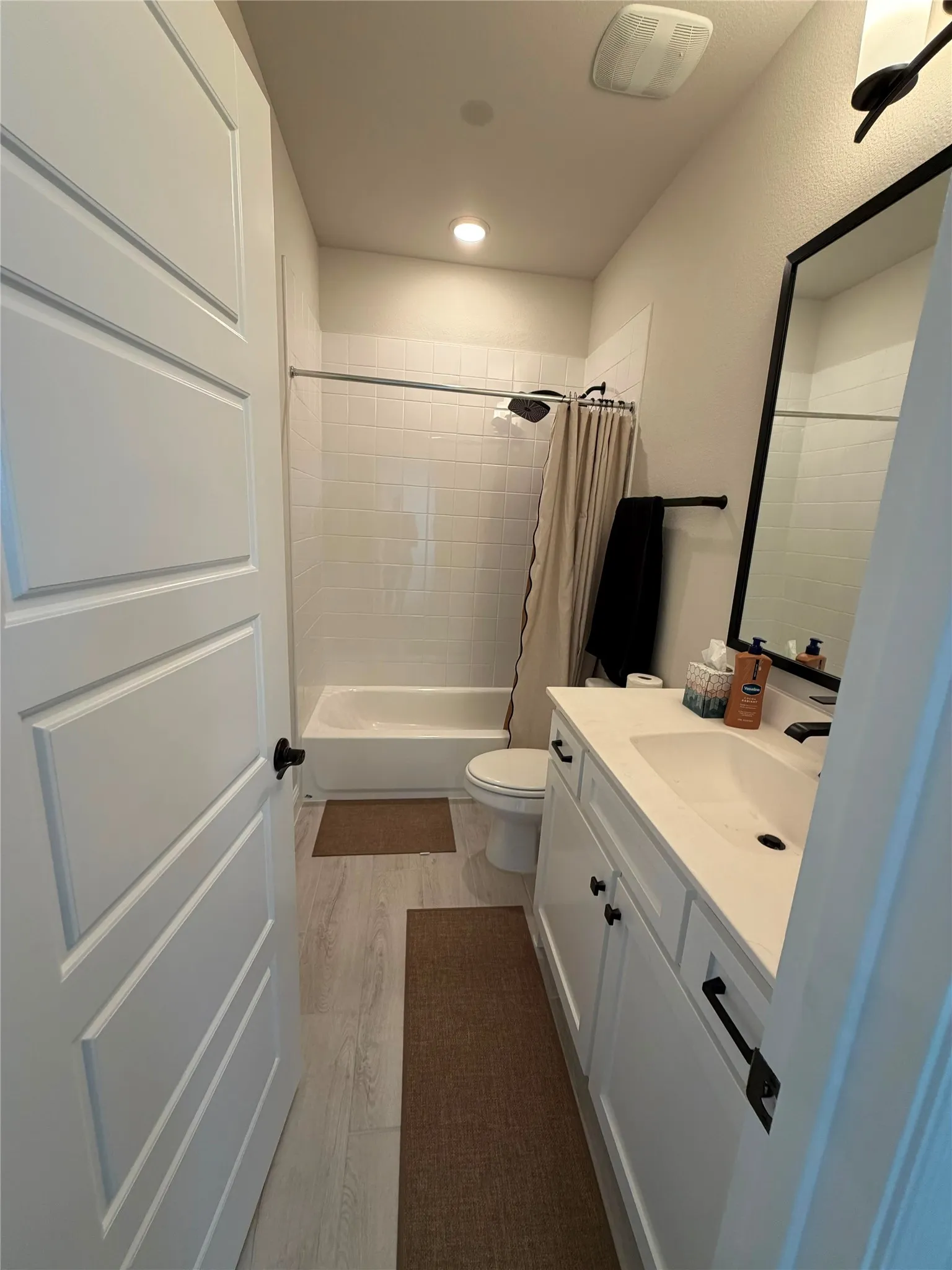 White vanity with undermount sink, black framed mirror, and wood-finish flooring