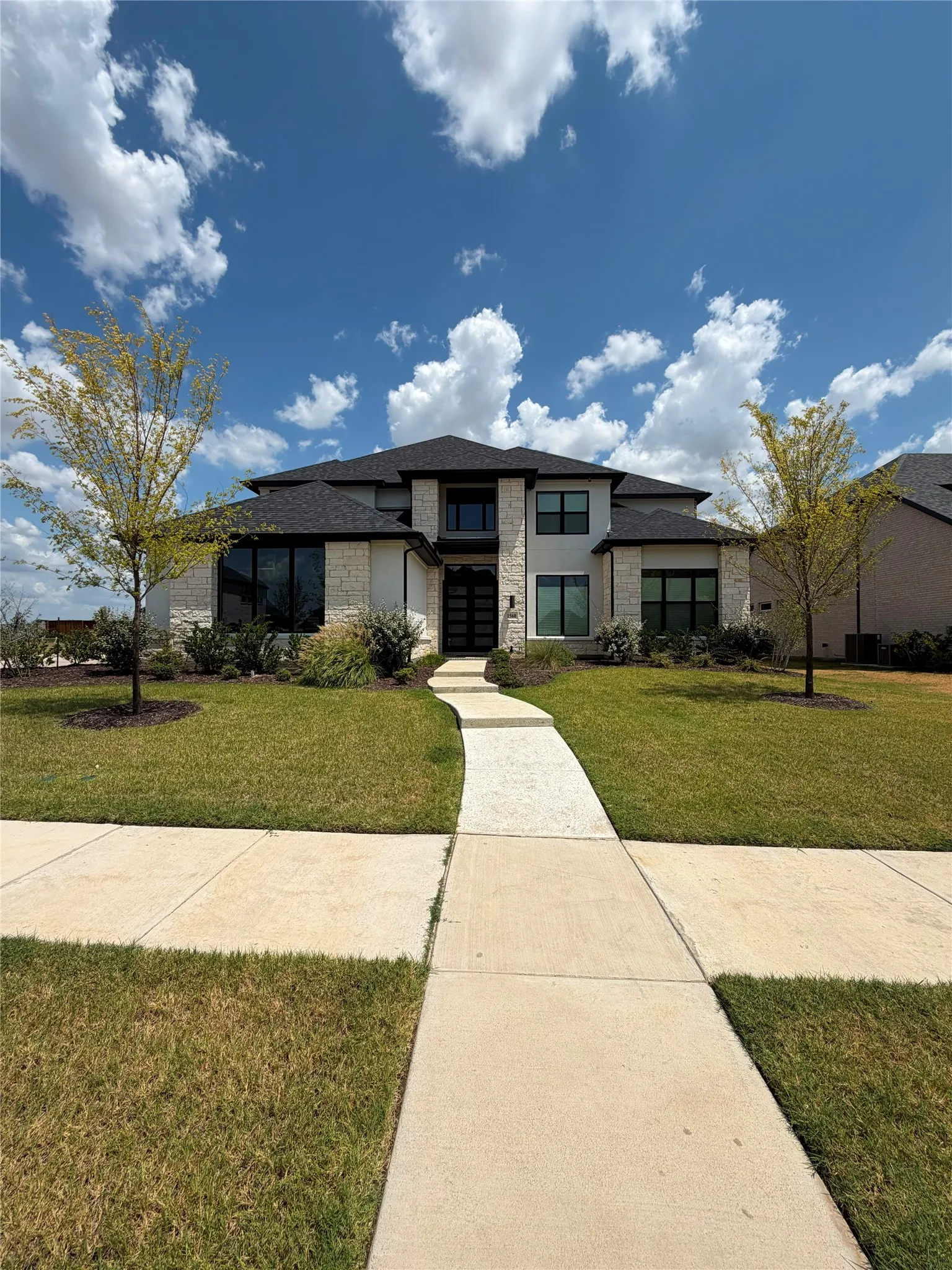 Contemporary architecture featuring a stone and stucco exterior, dark-framed windows, and a black shingle roof