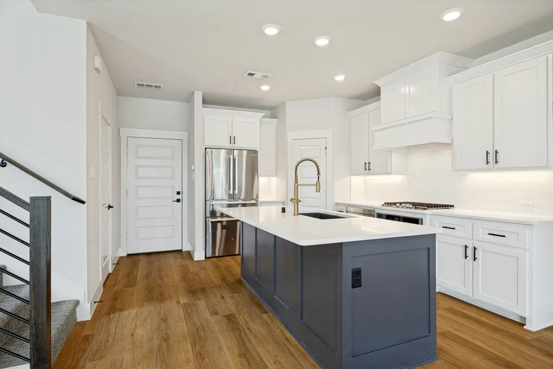 Gourmet kitchen featuring a large central island with a sink, stainless steel appliances, white cabinetry, and wood-finish flooring