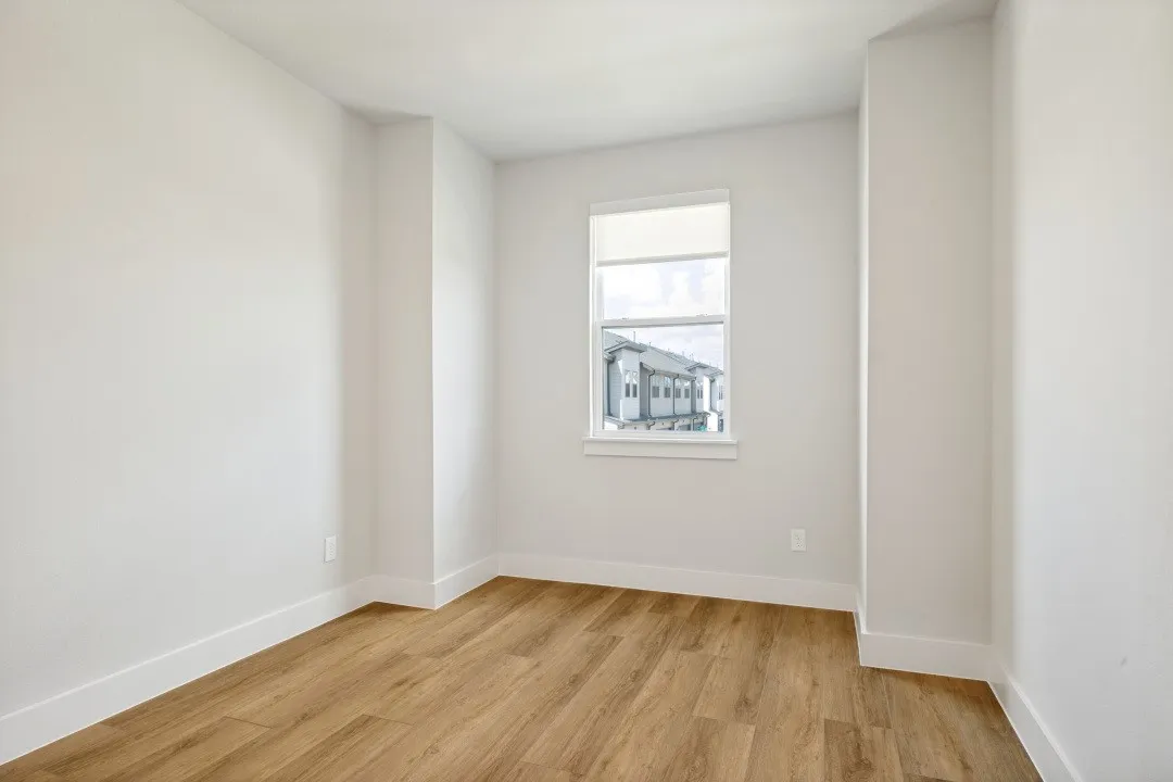 Wood-finish flooring, white walls, and a window with a roller shade
