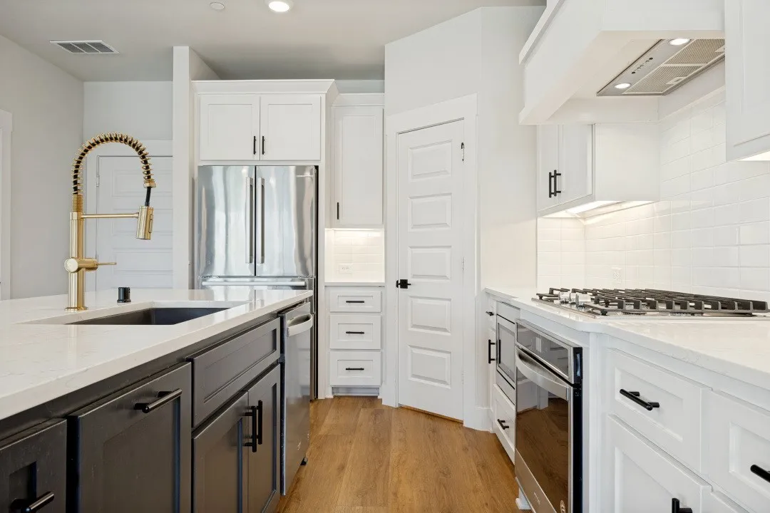 Chef's kitchen featuring stainless steel appliances, wood-finish flooring, white cabinetry, dark island cabinetry, and a gold-finish gooseneck faucet