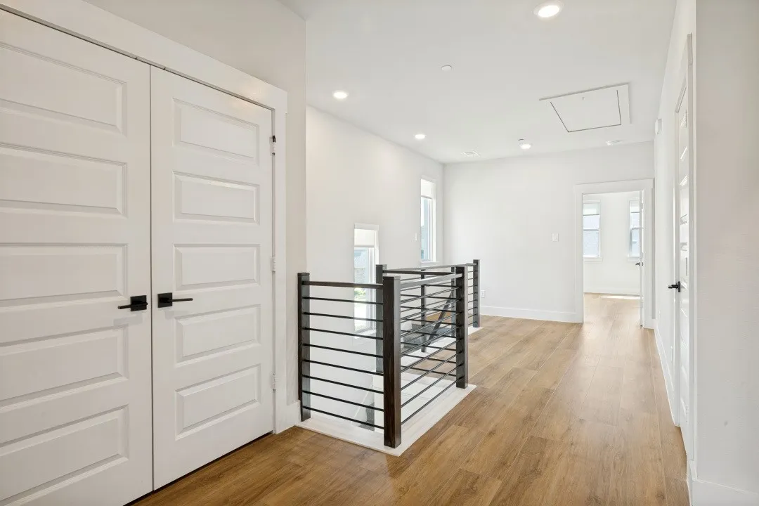 Wood-finish flooring, contemporary black metal railing, recessed lighting, and white paneled doors with black hardware