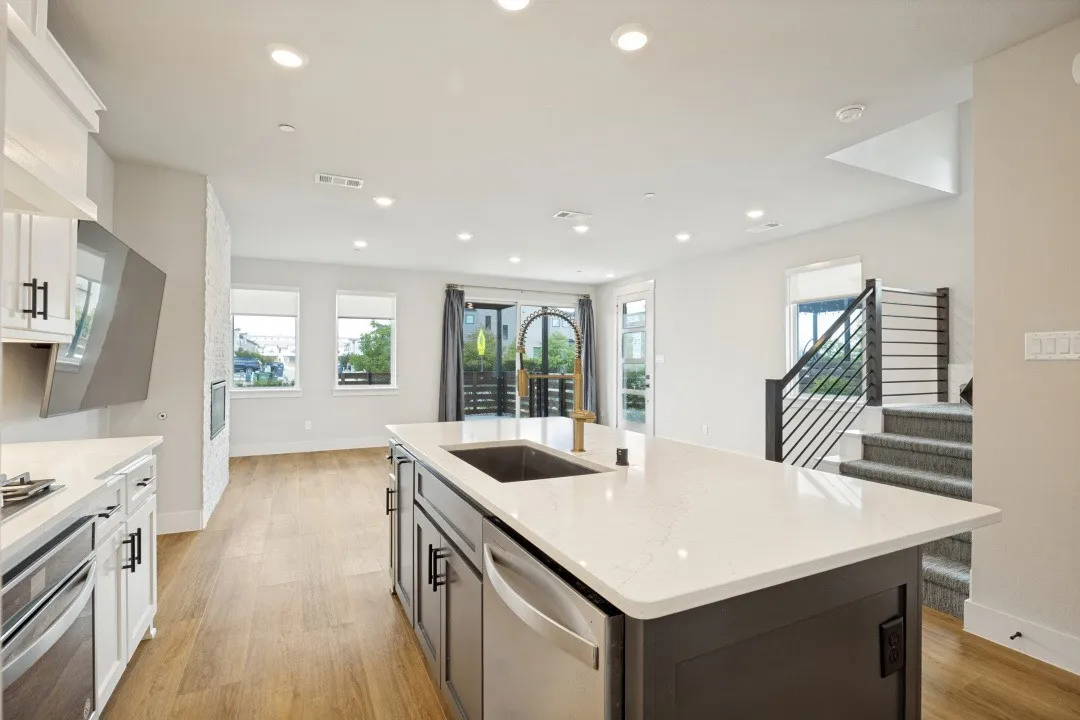 Open-concept living area with wood-finish flooring, a kitchen island with an integrated sink, recessed lighting, and a modern staircase with horizontal railings