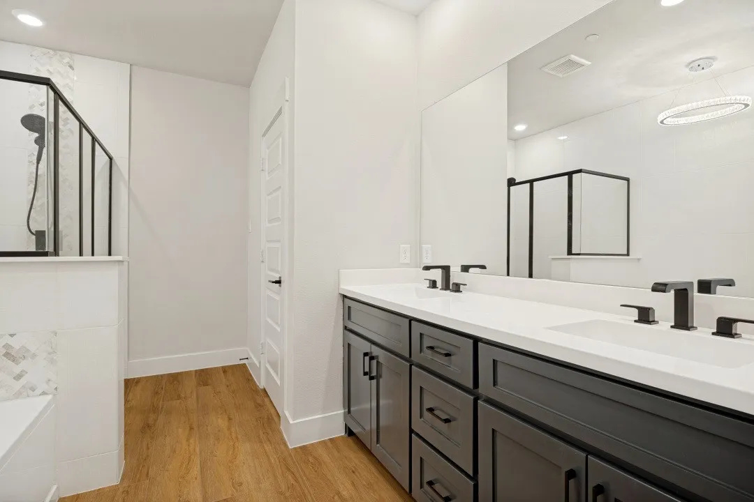 Dual vanity with undermount sinks, matte black fixtures, wood-finish flooring, and a glass-enclosed shower featuring a tiled bench