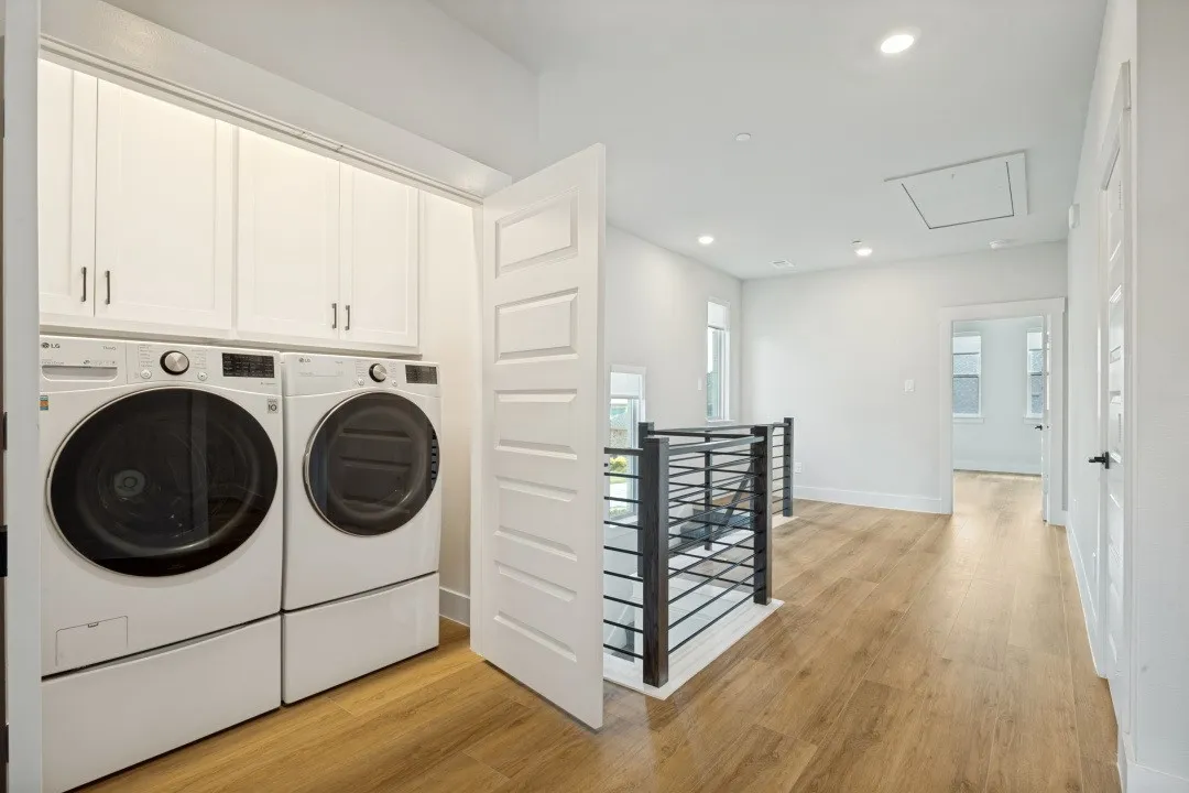 Laundry area with white cabinetry and appliances, wood-finish flooring, and a modern metal railing