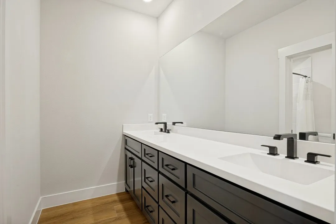 Dual vanity with integrated white rectangular sinks, matte black faucets, dark wood-finish cabinetry, and a full-width mirror