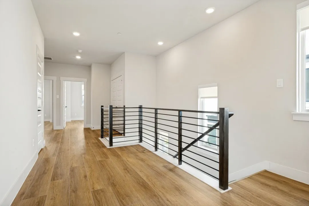 Upper-level landing featuring wood-finish flooring, recessed lighting, and a modern horizontal railing system