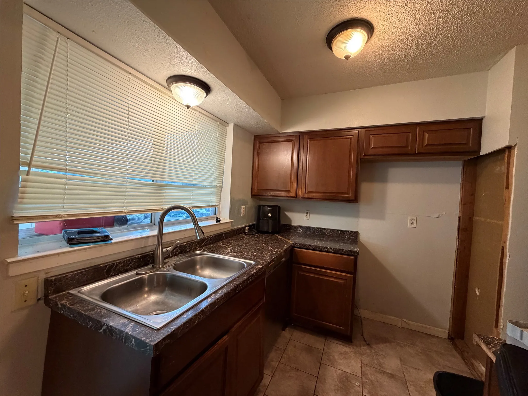 Double basin stainless steel sink with a gooseneck faucet, wood-finish cabinetry, and patterned countertops