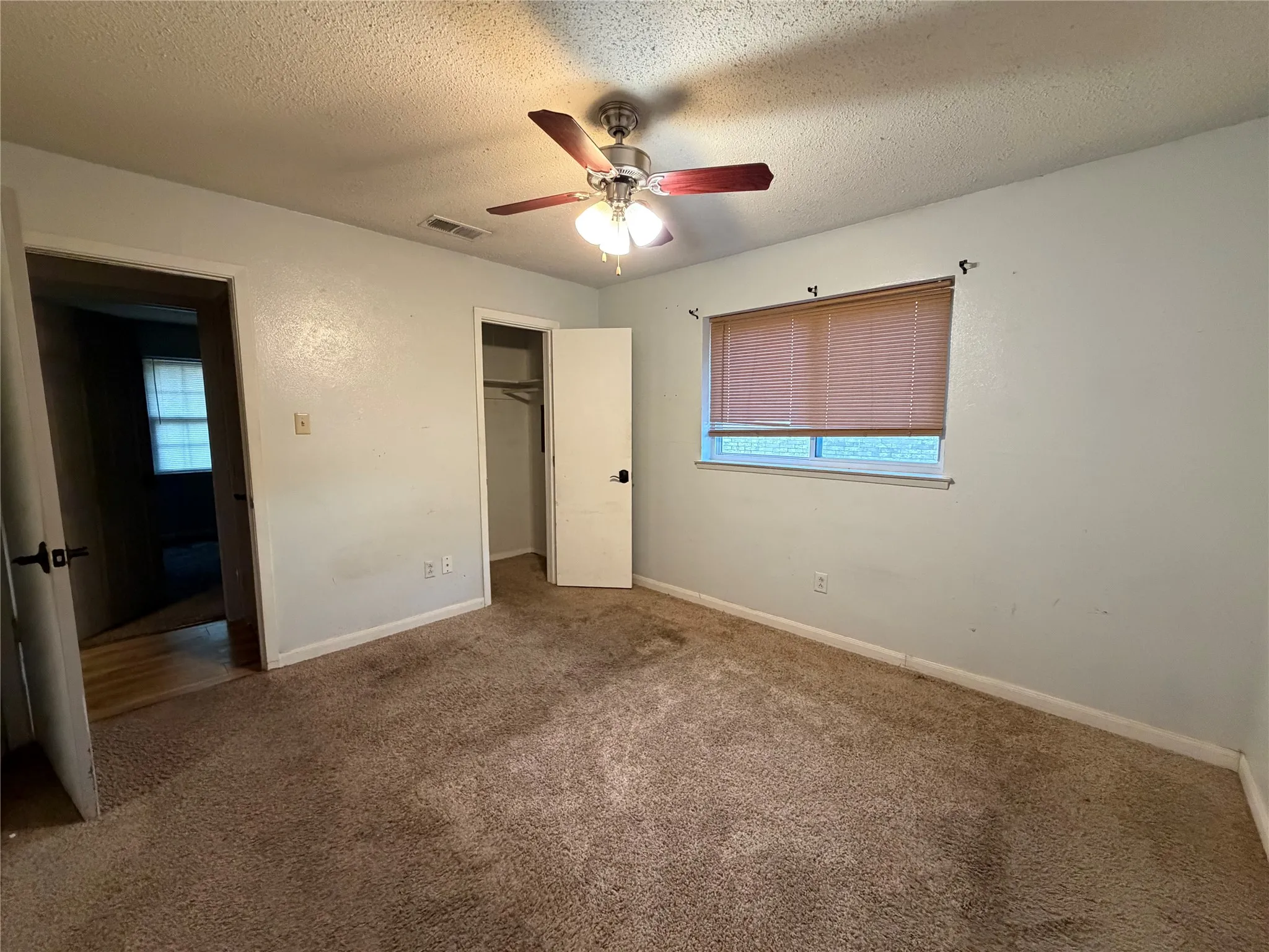 Ceiling fan with light fixture, window with blinds, brown carpeting, interior doors with dark hardware, and a closet