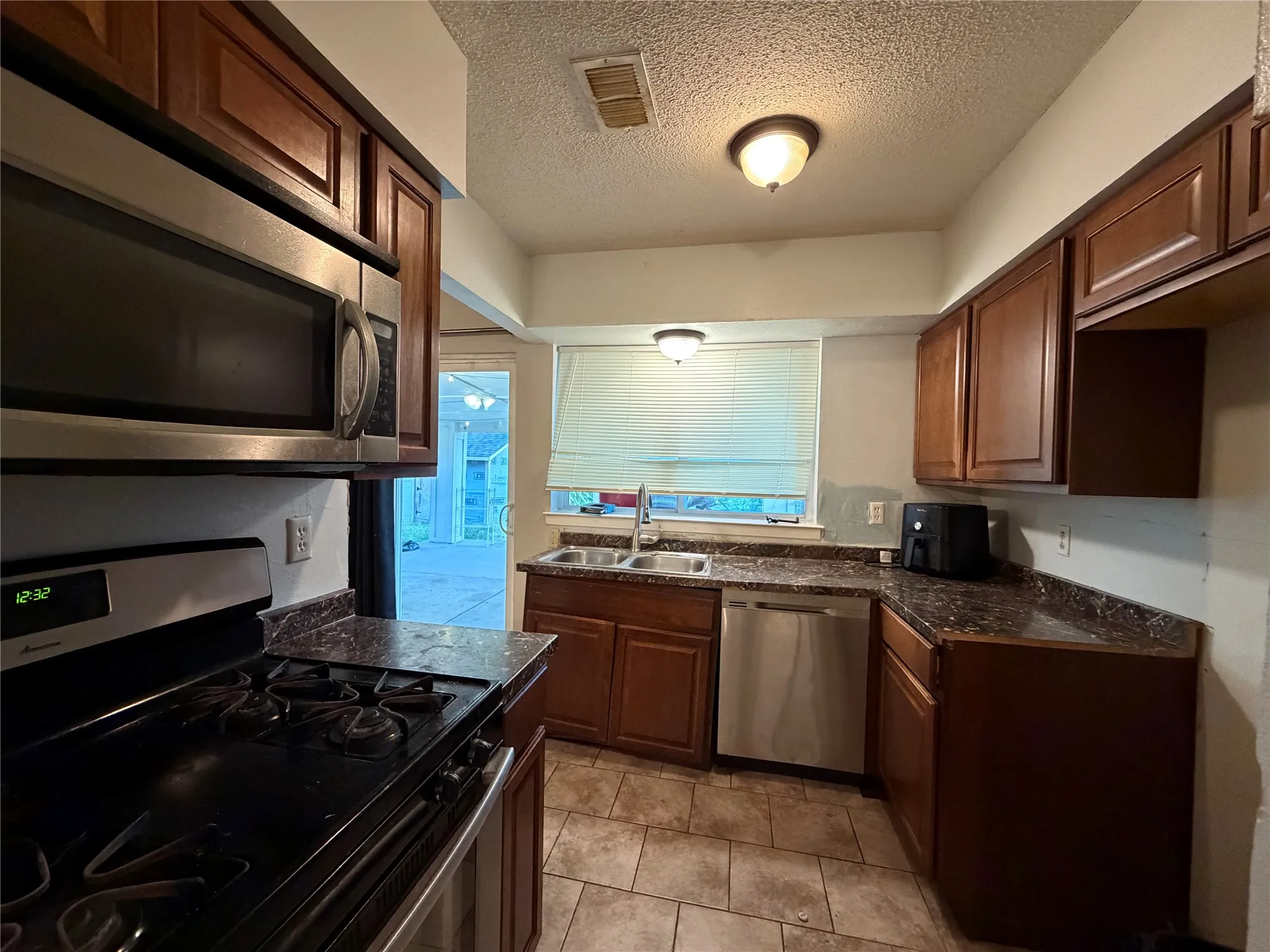 Kitchen featuring stainless steel appliances, wood cabinetry, stone-finish countertops, and tile flooring
