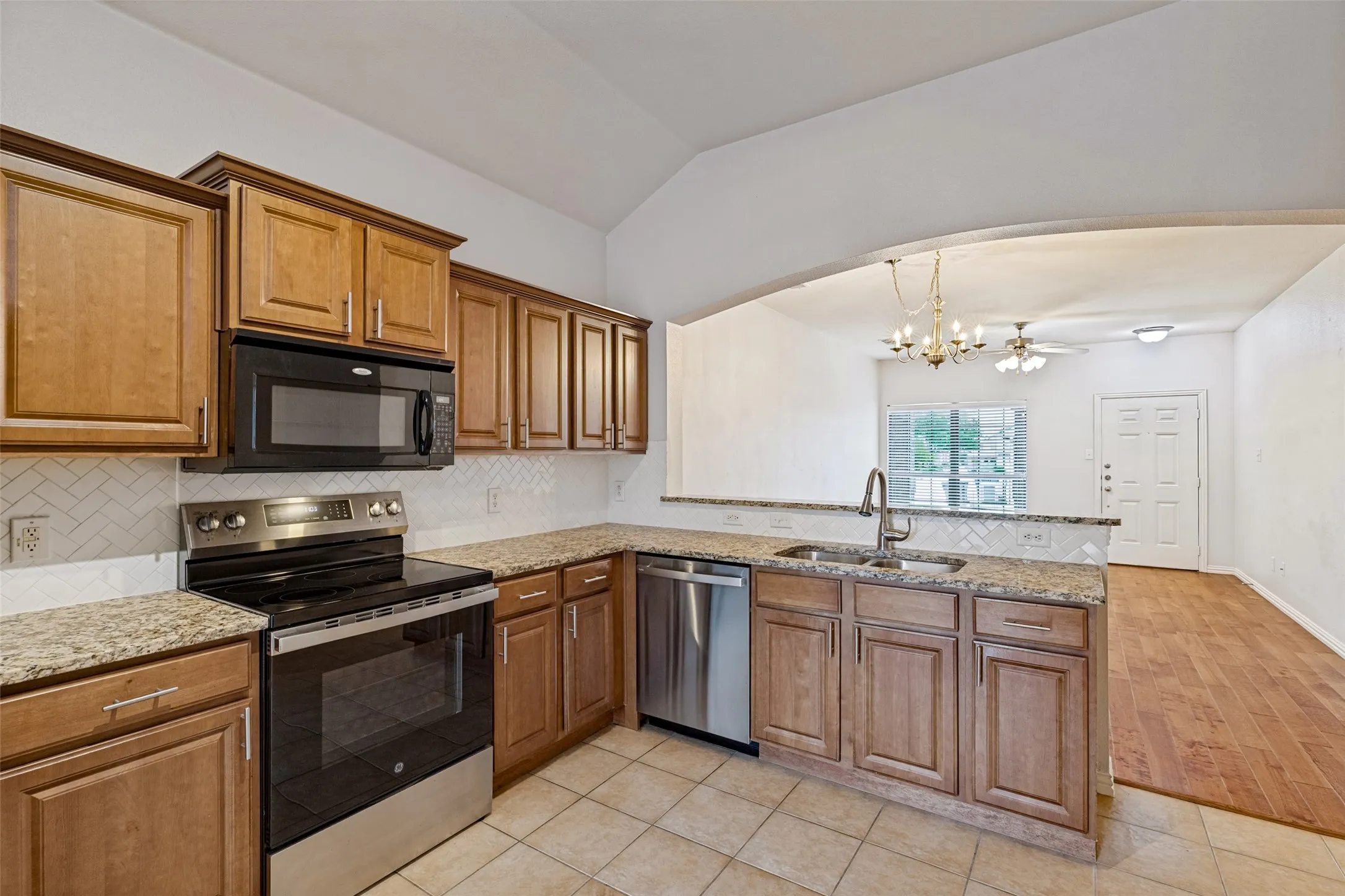 Kitchen featuring light wood cabinetry, stone countertops, stainless steel appliances, a white tile backsplash, and a double basin sink