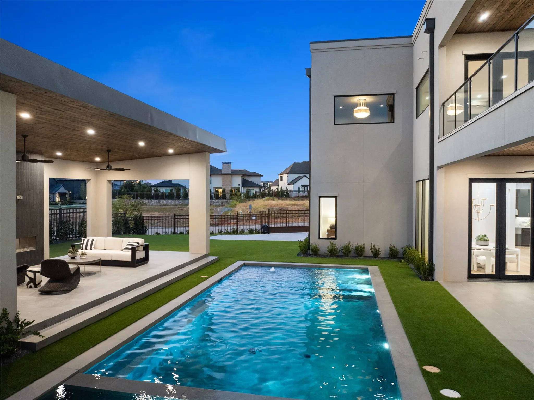 Swimming pool with integrated lighting, a covered outdoor living area featuring a wood-finish ceiling, and a second-story balcony with glass railing