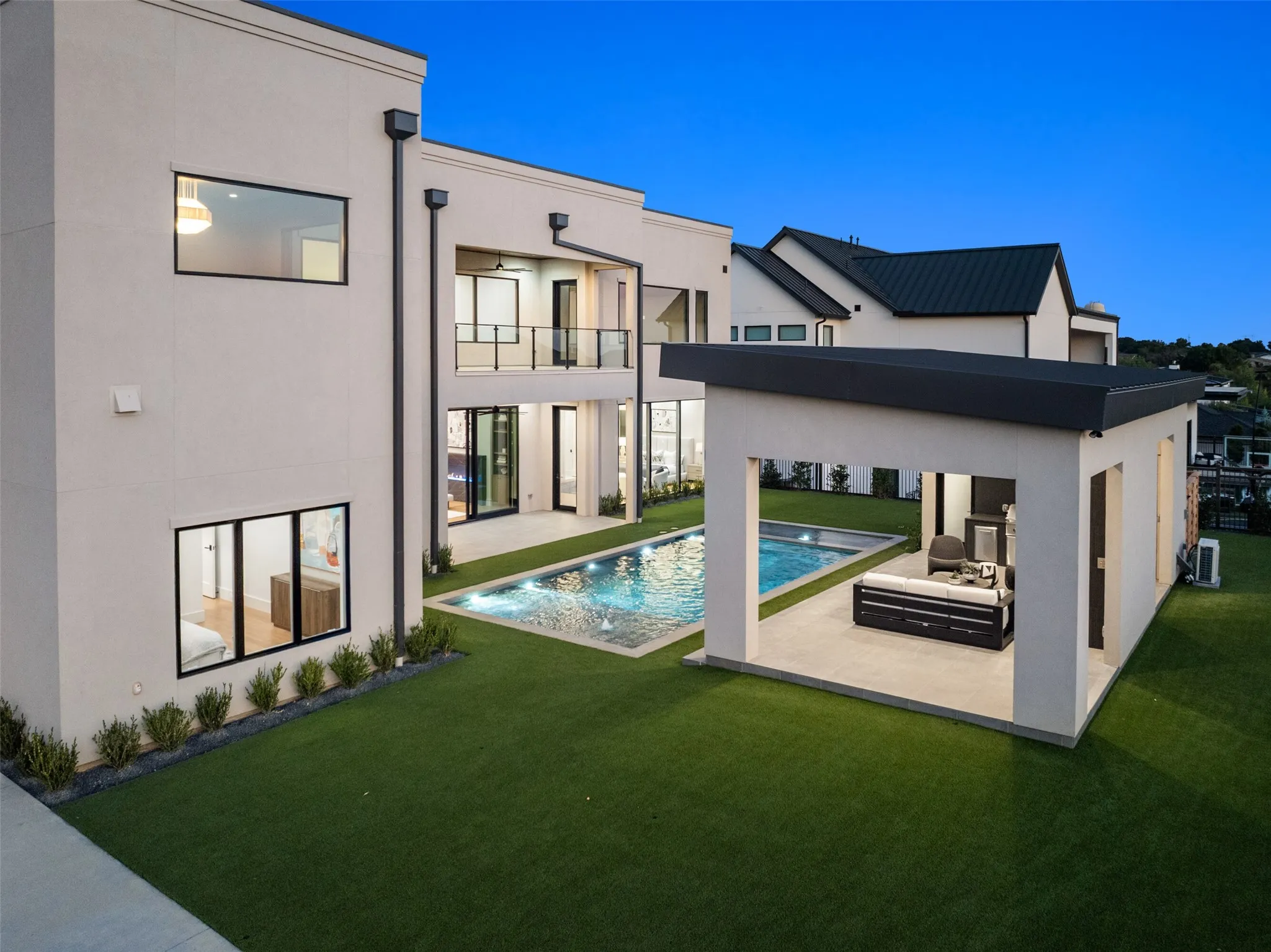Modern stucco exterior with black-framed windows, a glass-railed balcony, an in-ground swimming pool, and a covered patio structure