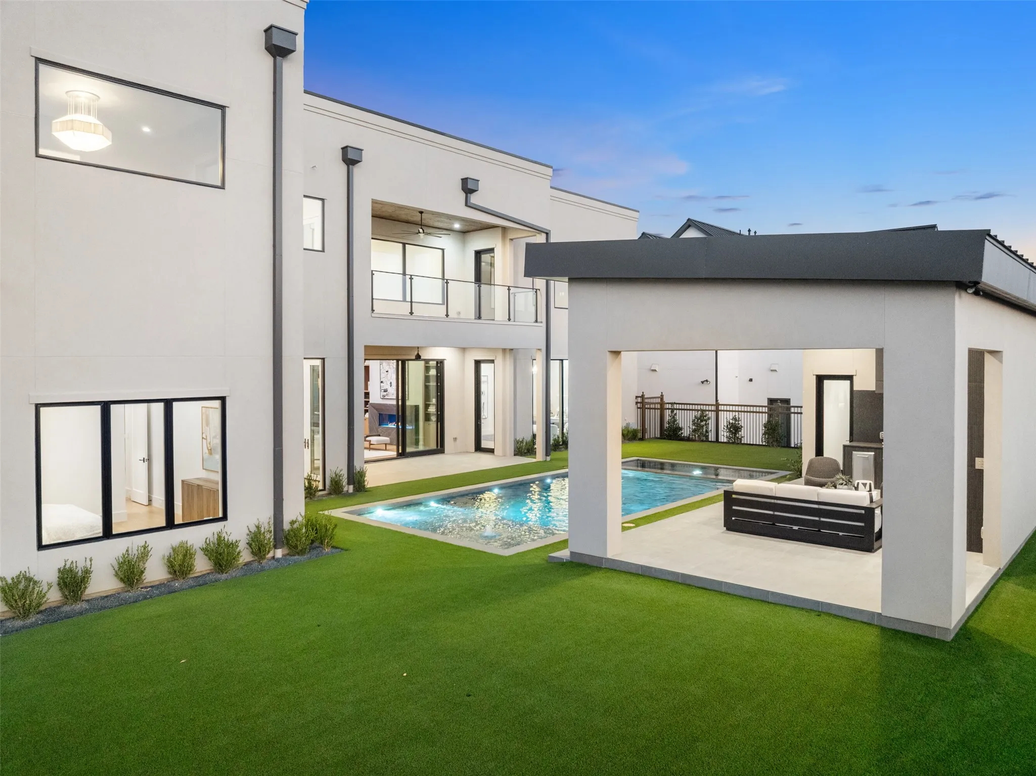 Modern exterior with expansive artificial turf, a rectangular swimming pool, and a covered outdoor living area featuring a built-in counter
