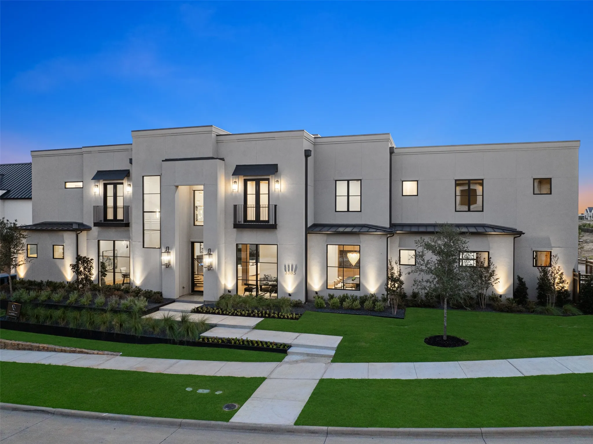 Modern stucco exterior with black-framed windows, prominent entry, and multiple exterior wall sconces