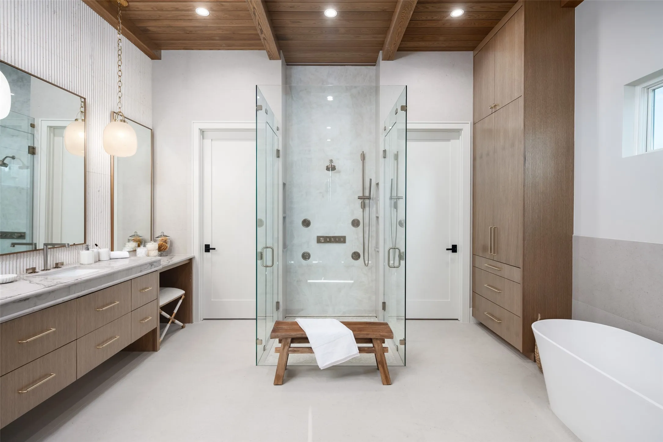 Dual vanity with stone countertop, large walk-in shower with multiple showerheads, freestanding soaking tub, and natural wood ceiling with exposed beams