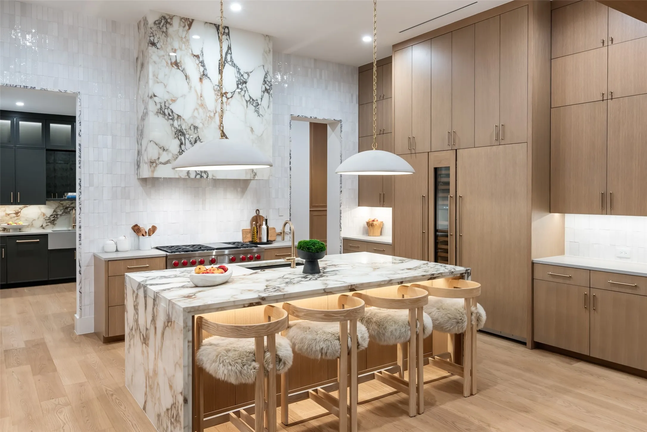 Waterfall island with integrated seating, range hood, light wood-finish cabinetry, built-in wine refrigeration.