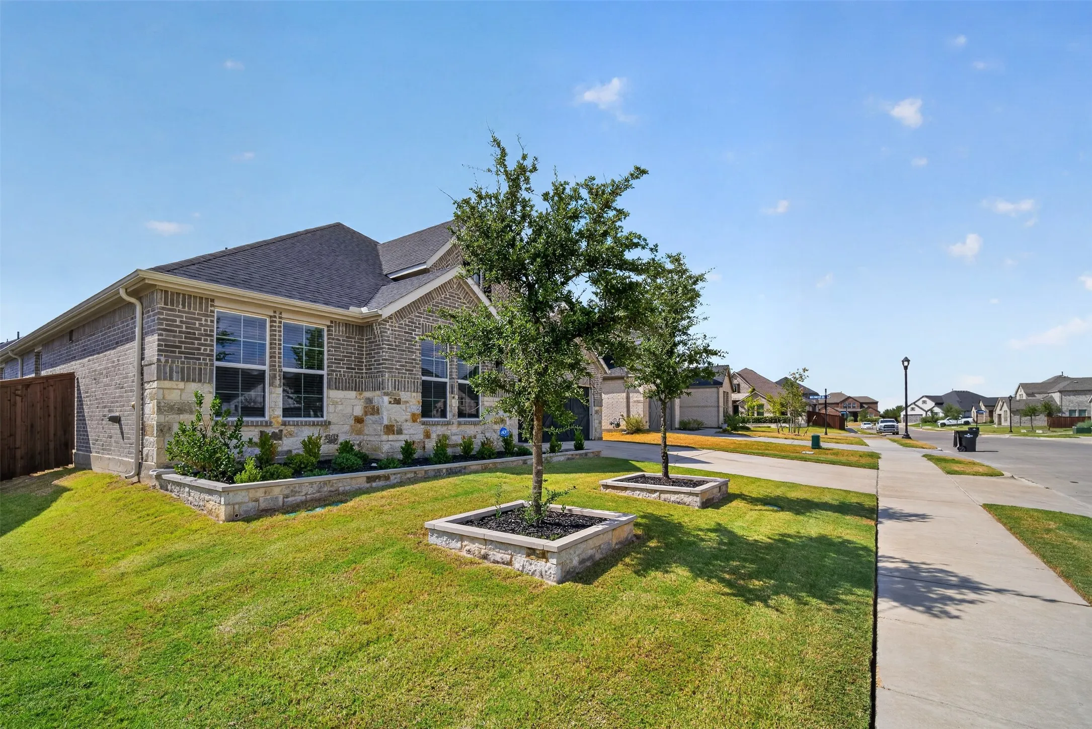 Brick and stone facade, landscaped planting beds, mature trees, concrete sidewalk, asphalt street