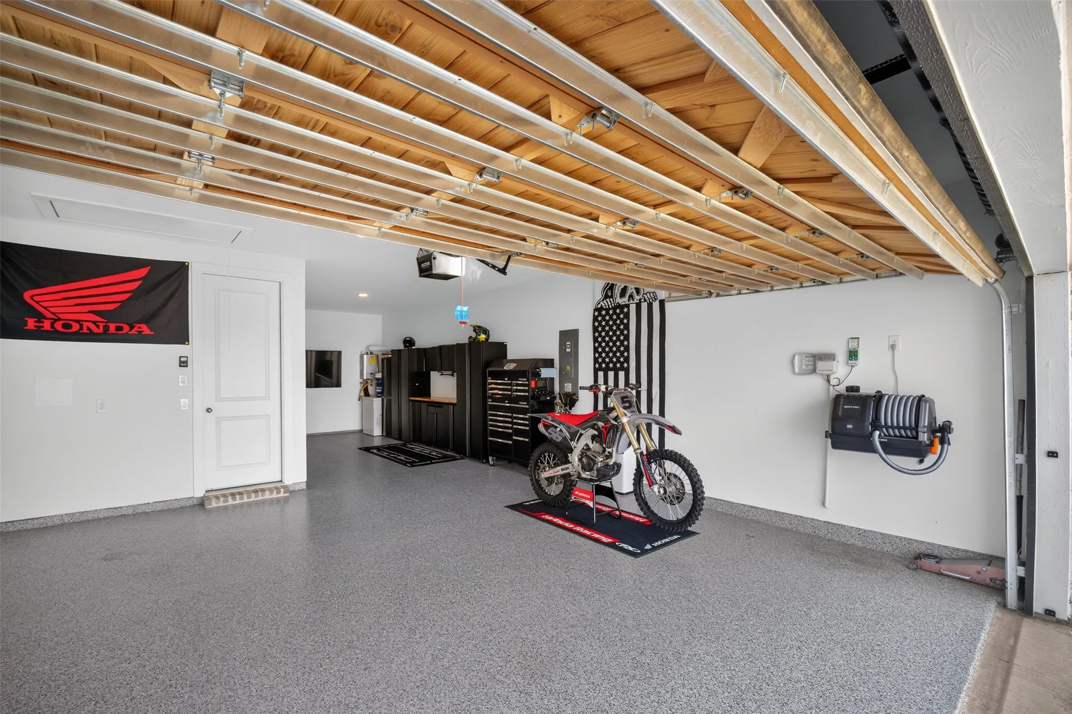 Garage featuring an epoxy coated floor, exposed wood ceiling, white walls, and built-in storage cabinetry