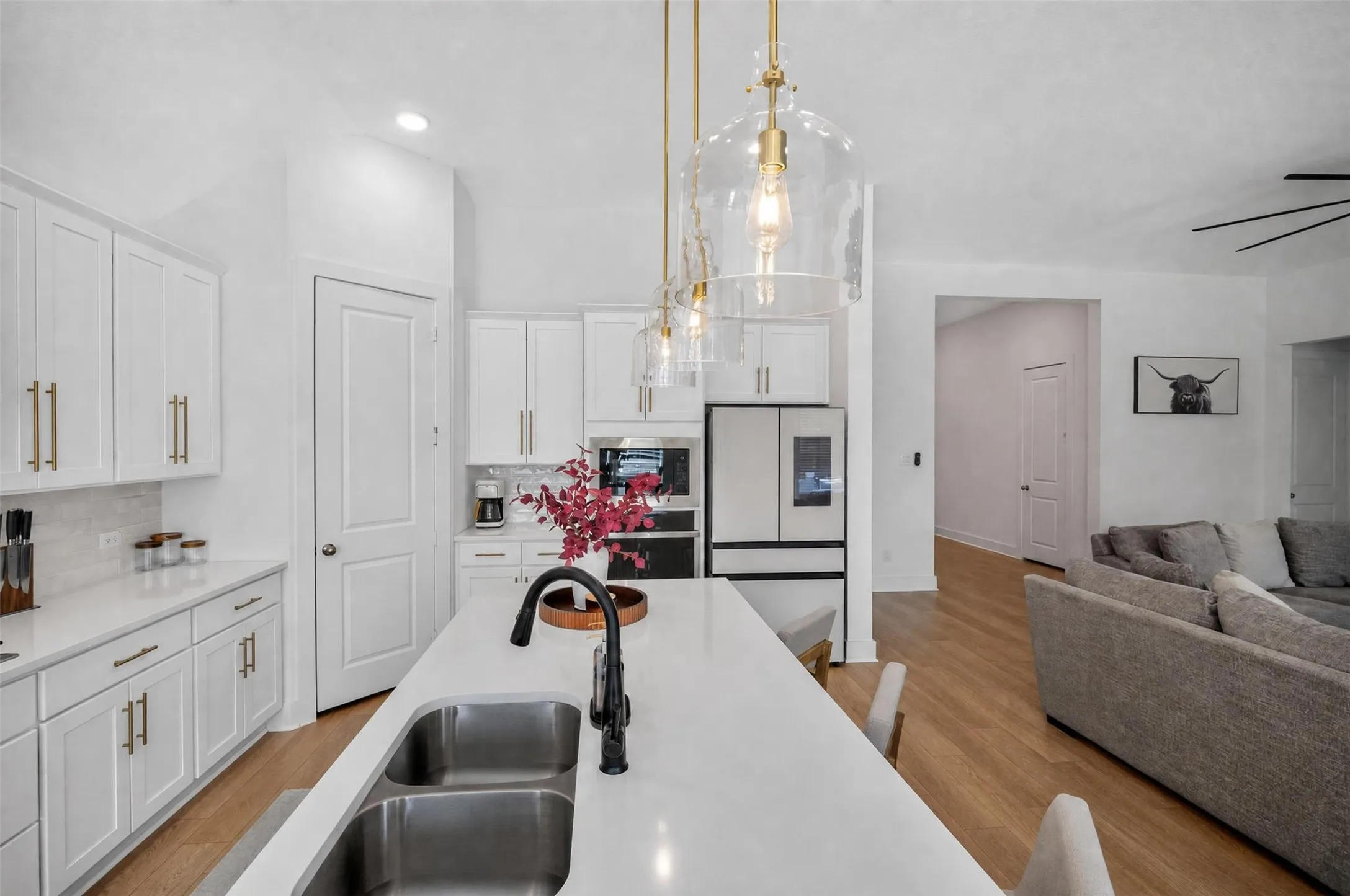 Kitchen featuring a large island with dual-basin sink, white cabinetry with gold-finish hardware, stainless steel appliances, and wood-finish flooring