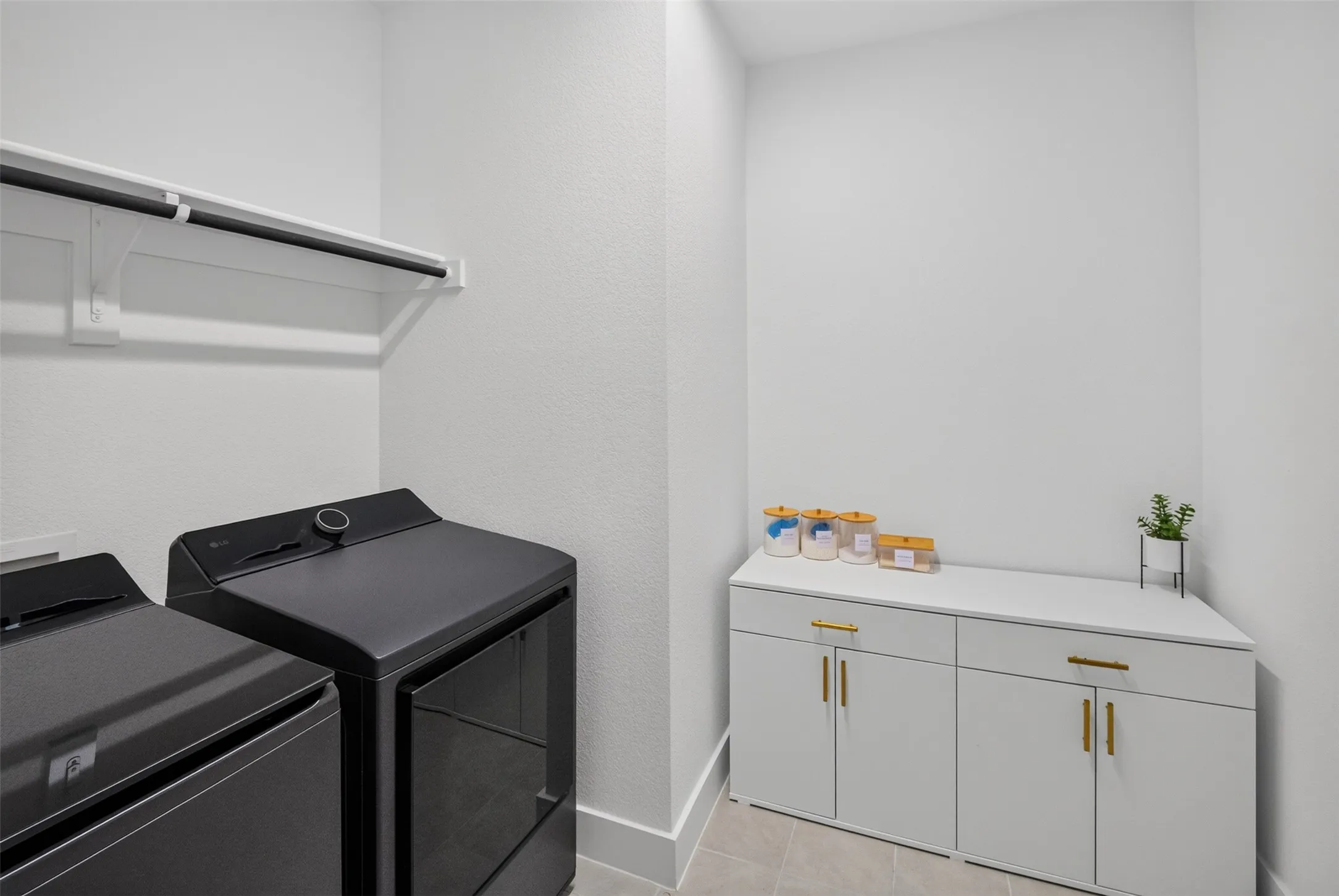 Laundry area featuring a built-in shelf with hanging rod, tile flooring, and white cabinetry with gold-tone hardware
