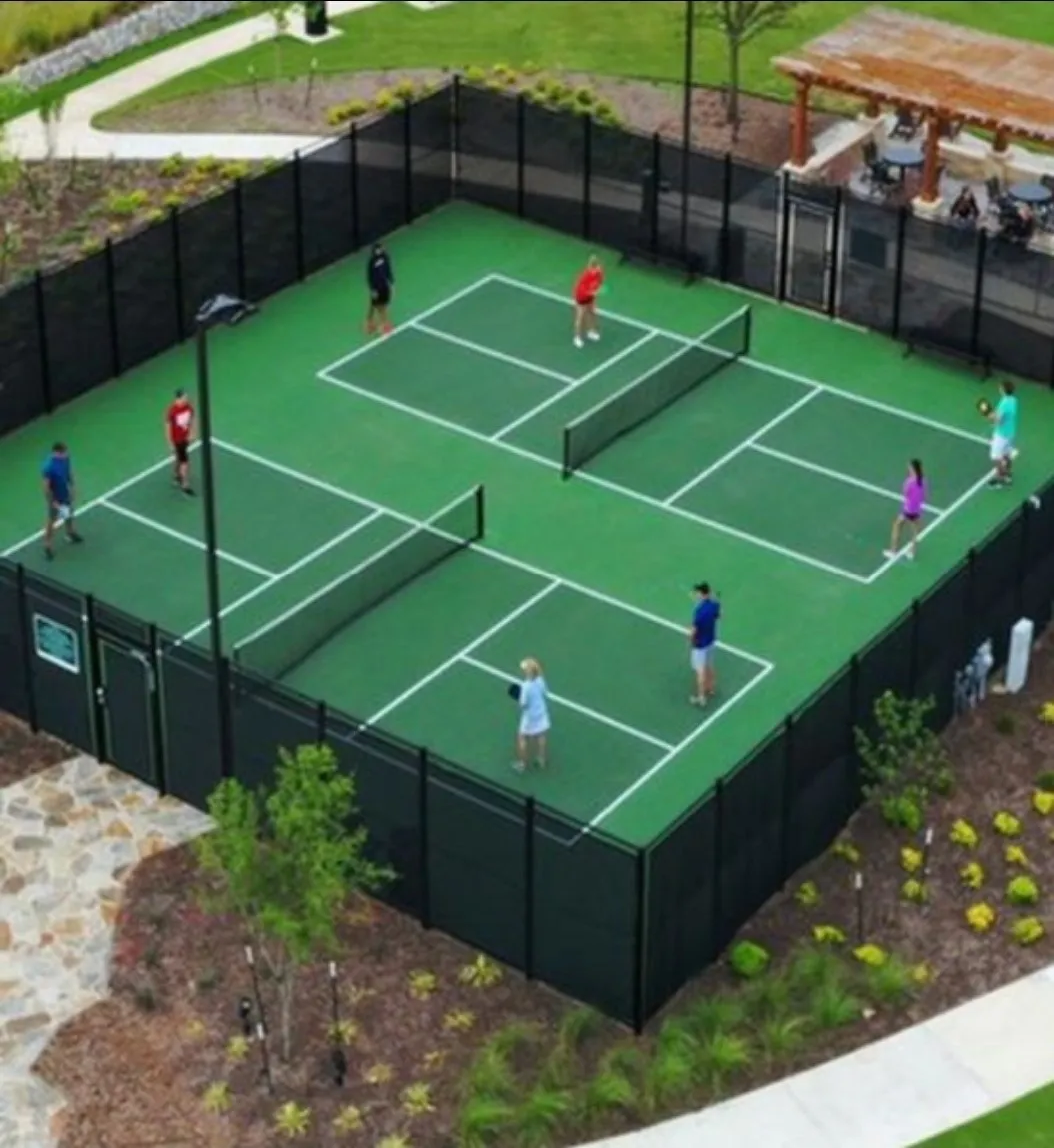 Gated multi-court pickleball facility with overhead lighting and adjacent pergola-covered seating