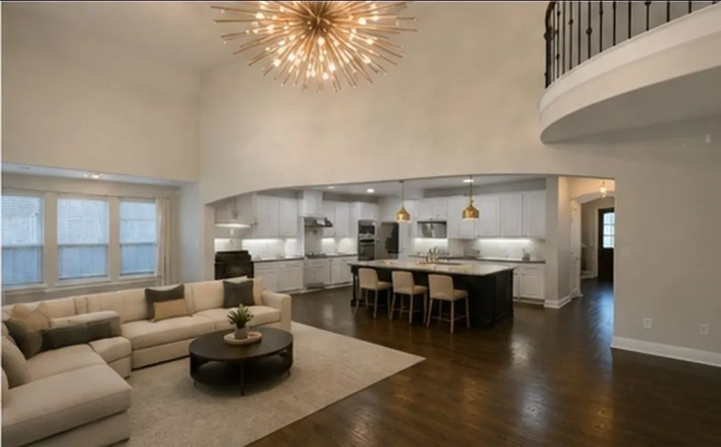 Soaring ceilings with an ornate light fixture, dark wood-finish flooring, and a kitchen featuring white cabinetry, a large island, and pendant lighting