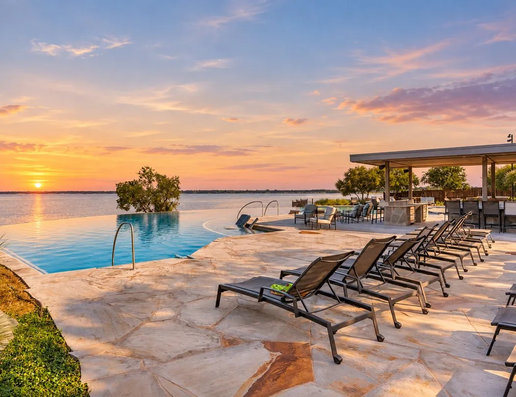 Infinity-edge pool, expansive flagstone patio, covered outdoor entertaining area, built-in outdoor kitchen, and waterfront access