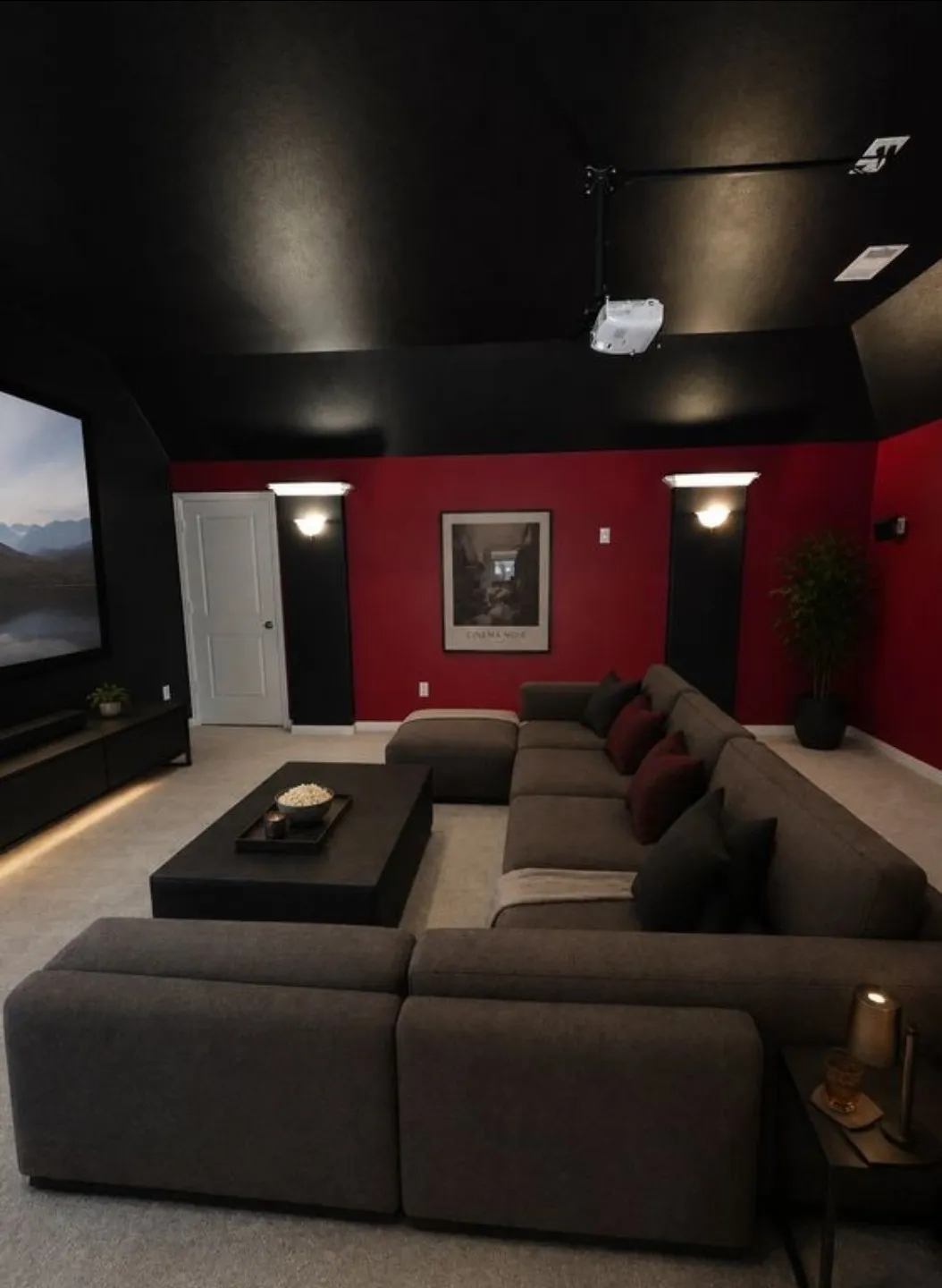 Media room featuring a projector, large screen, red accent wall, and recessed wall sconces