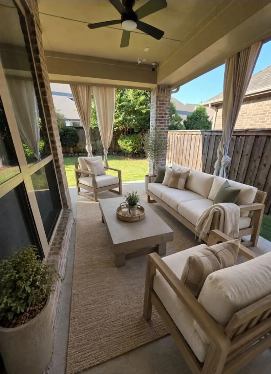 Covered patio featuring a ceiling fan, brick columns, concrete flooring, and privacy curtains