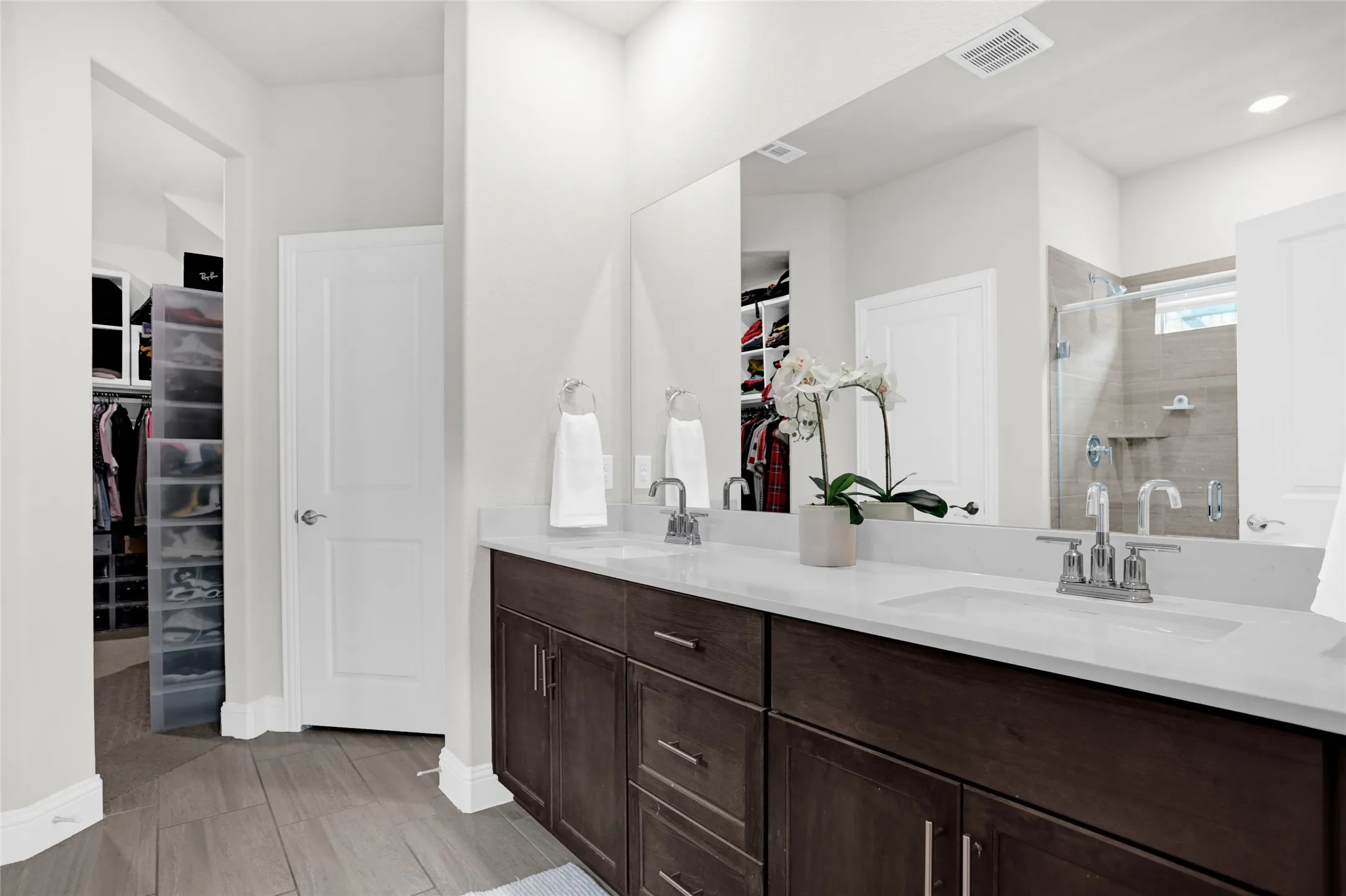 Full bath featuring a spacious closet, a shower stall, double vanity, and light wood-type flooring