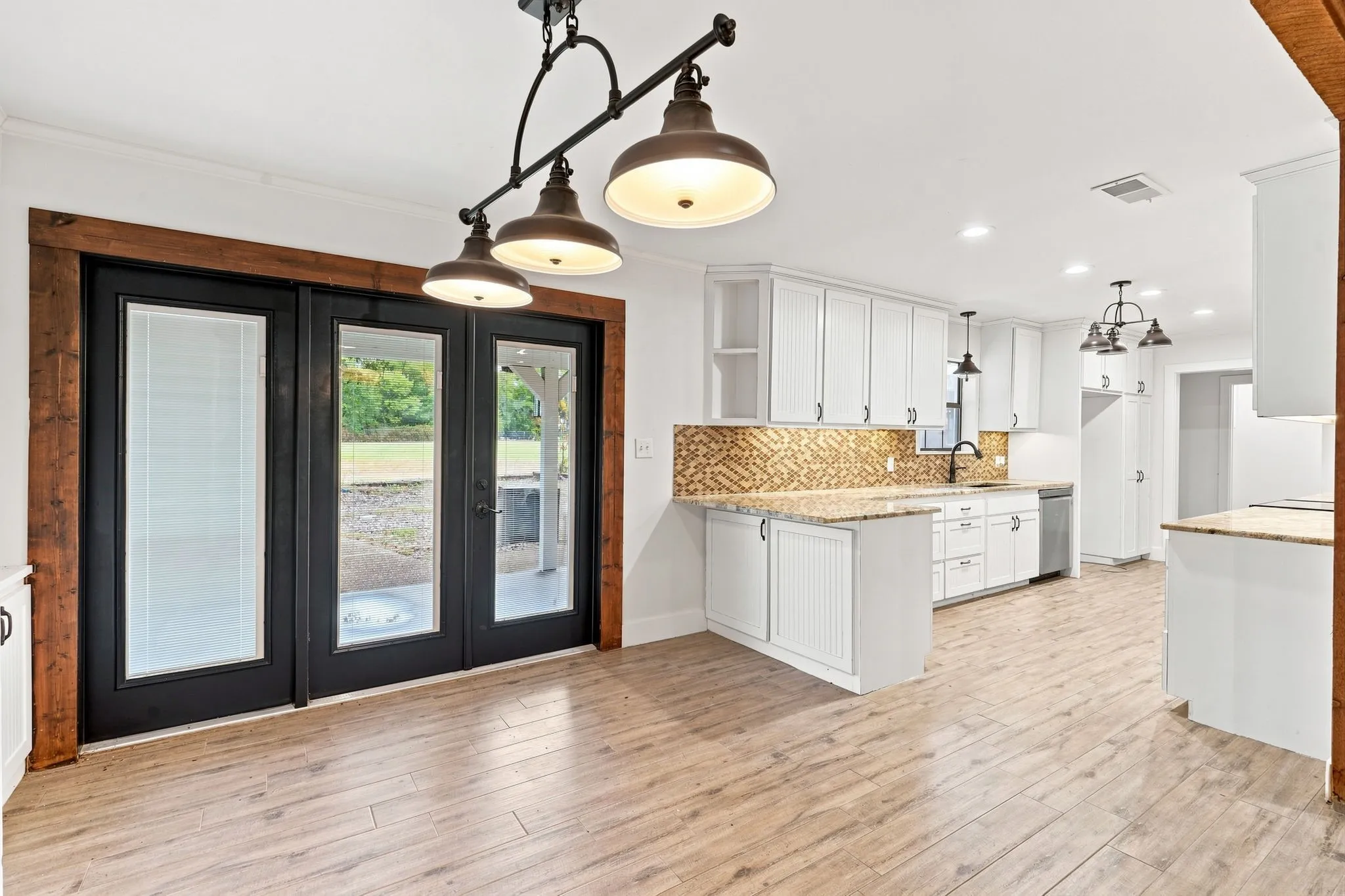 White cabinetry, wood-finish flooring, decorative backsplash, island with stone-finish countertop, and black frame glass doors