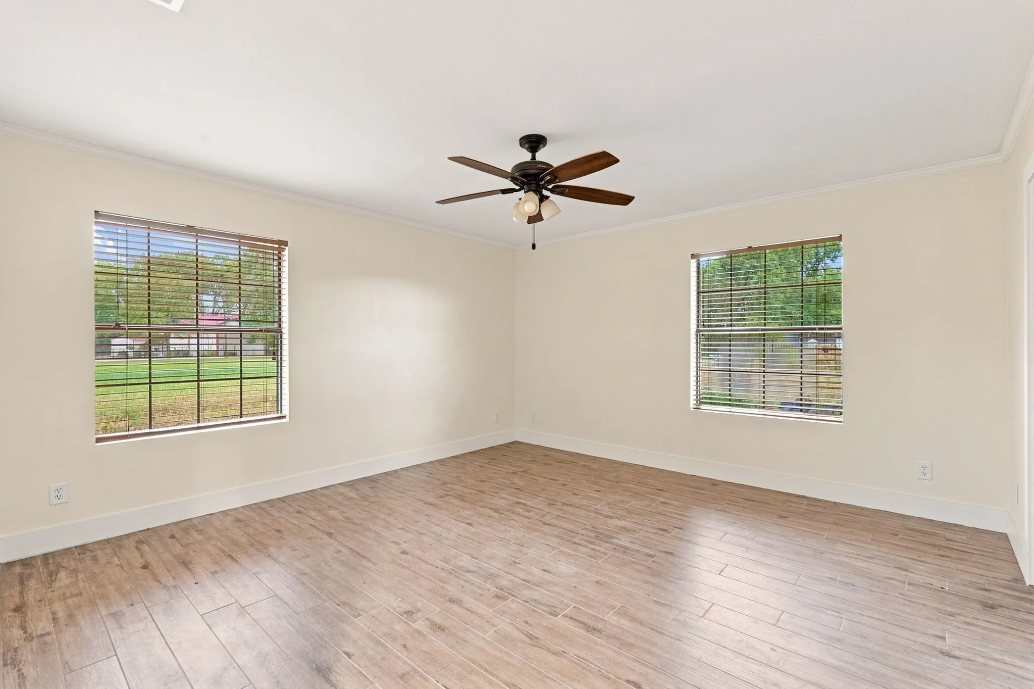 Spacious room featuring wood-finish flooring, two large windows with blinds, a ceiling fan, and crown molding