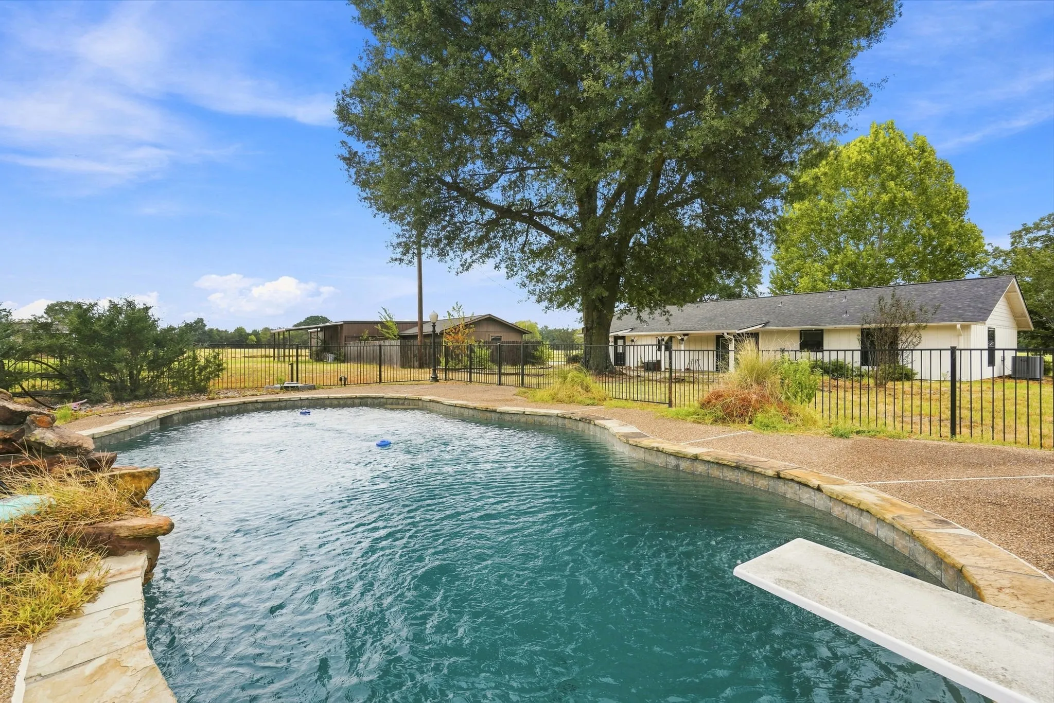 Curved swimming pool with a diving board, stone coping, and a surrounding aggregate deck