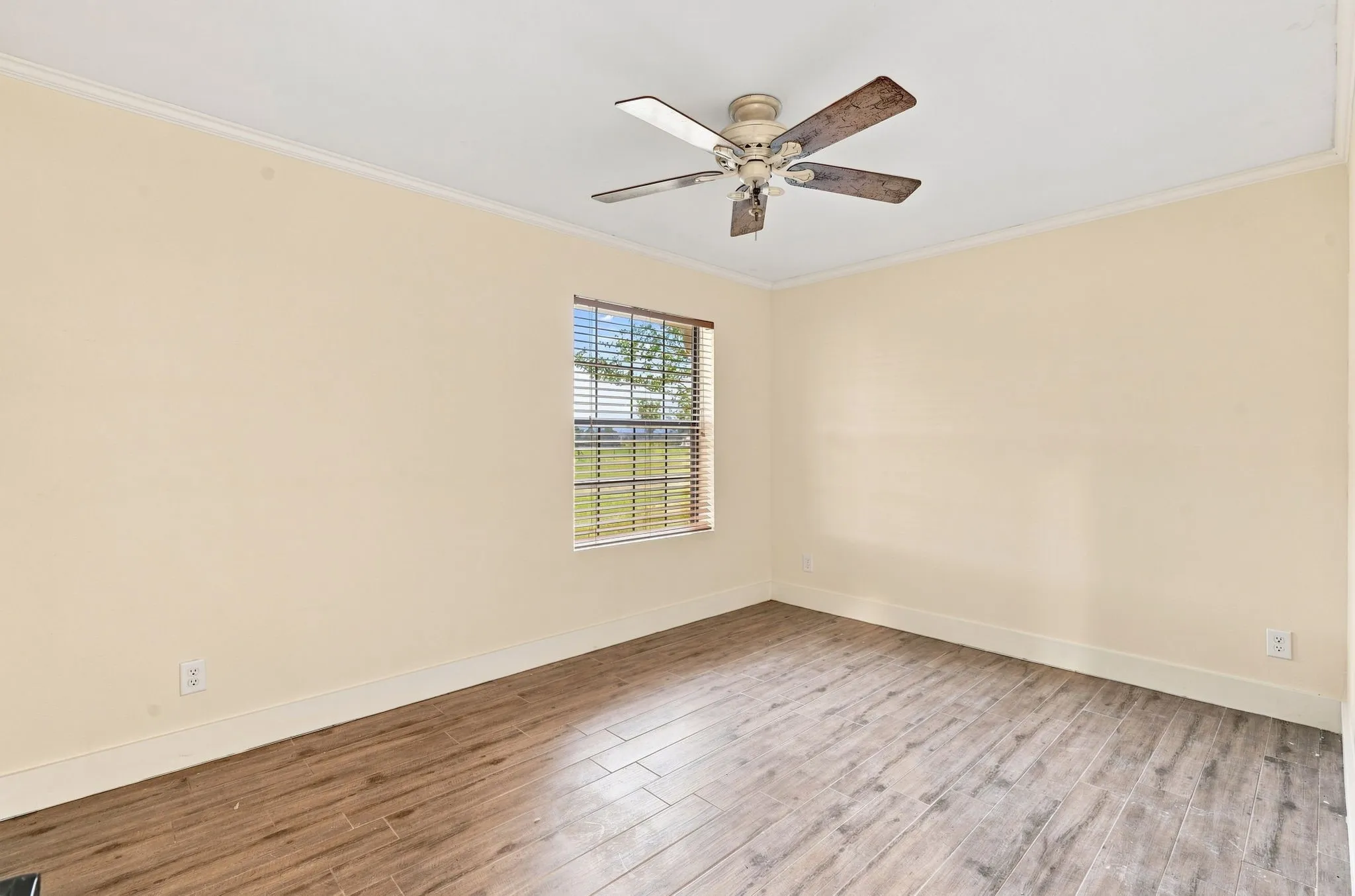 Wood-finish flooring, light-toned walls, a window with horizontal blinds, and a ceiling fan with wood-look blades