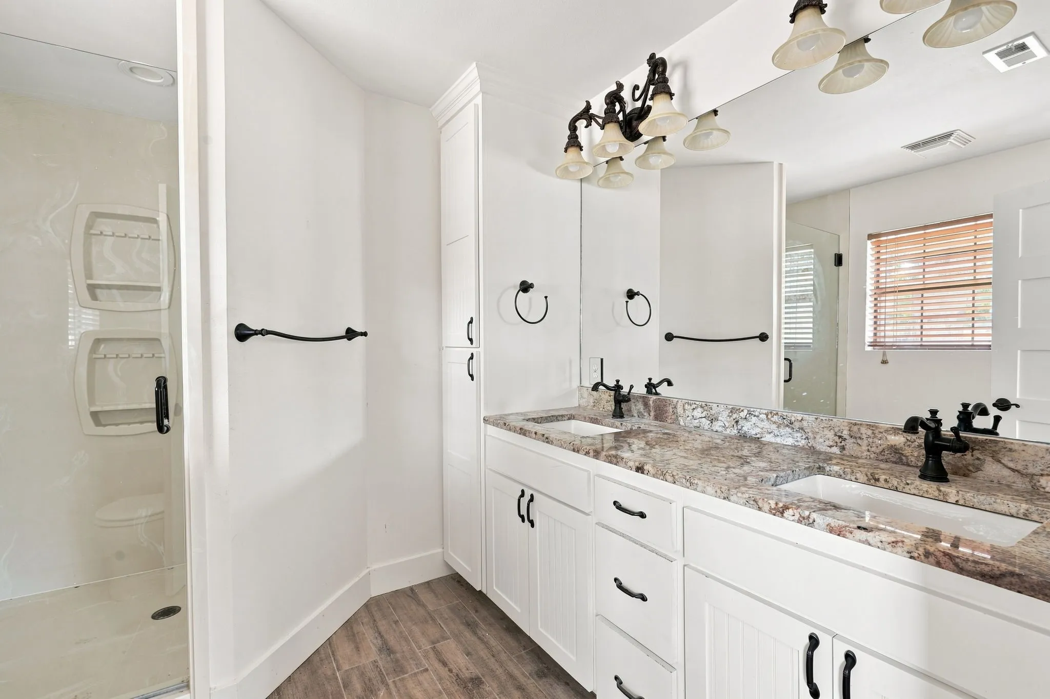 Dual vanity with stone countertop, white shaker cabinetry, wood-finish flooring, walk-in shower, and built-in storage
