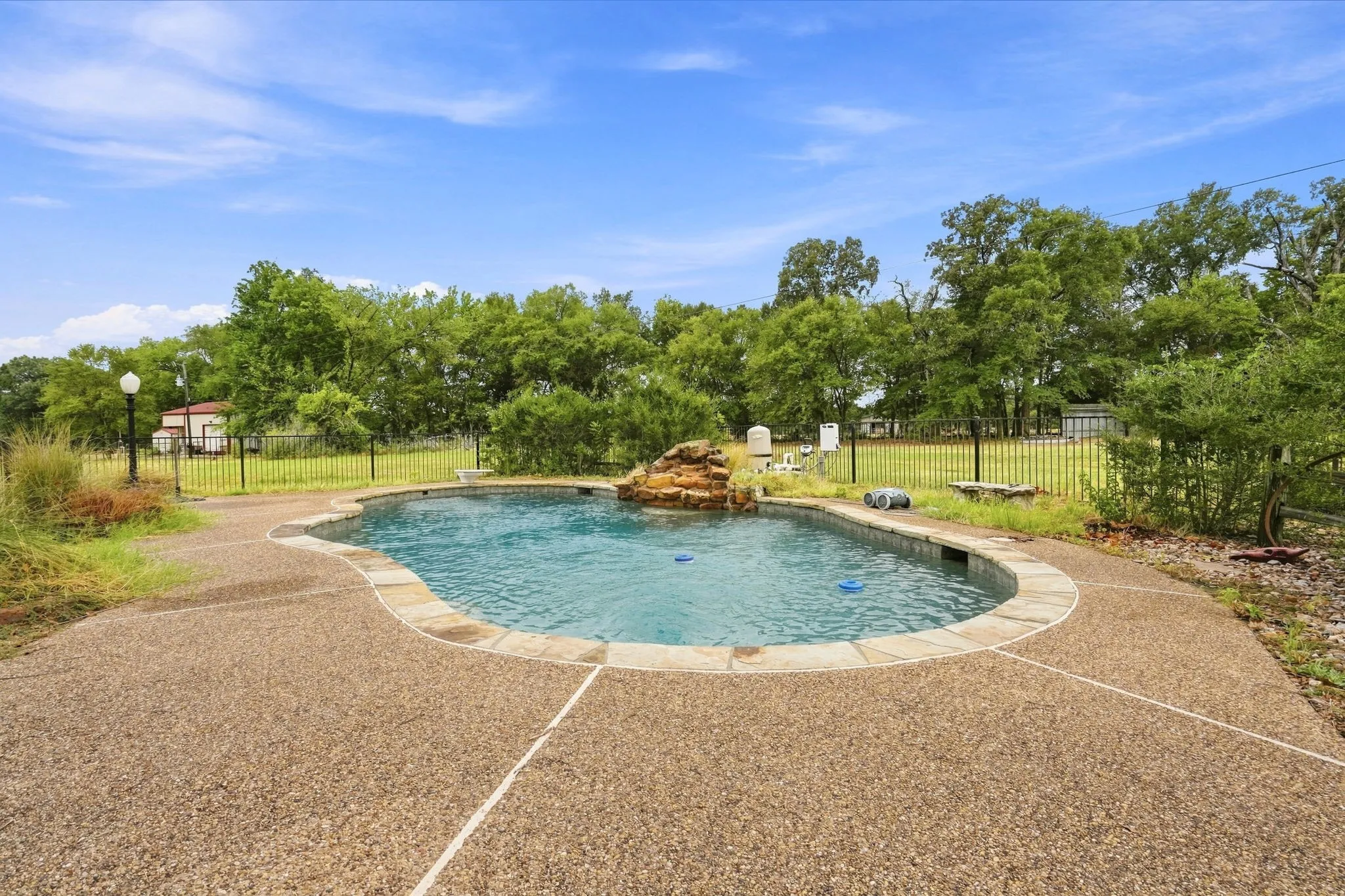 Curved swimming pool with a rock waterfall feature, bordered by stone coping and an exposed aggregate deck
