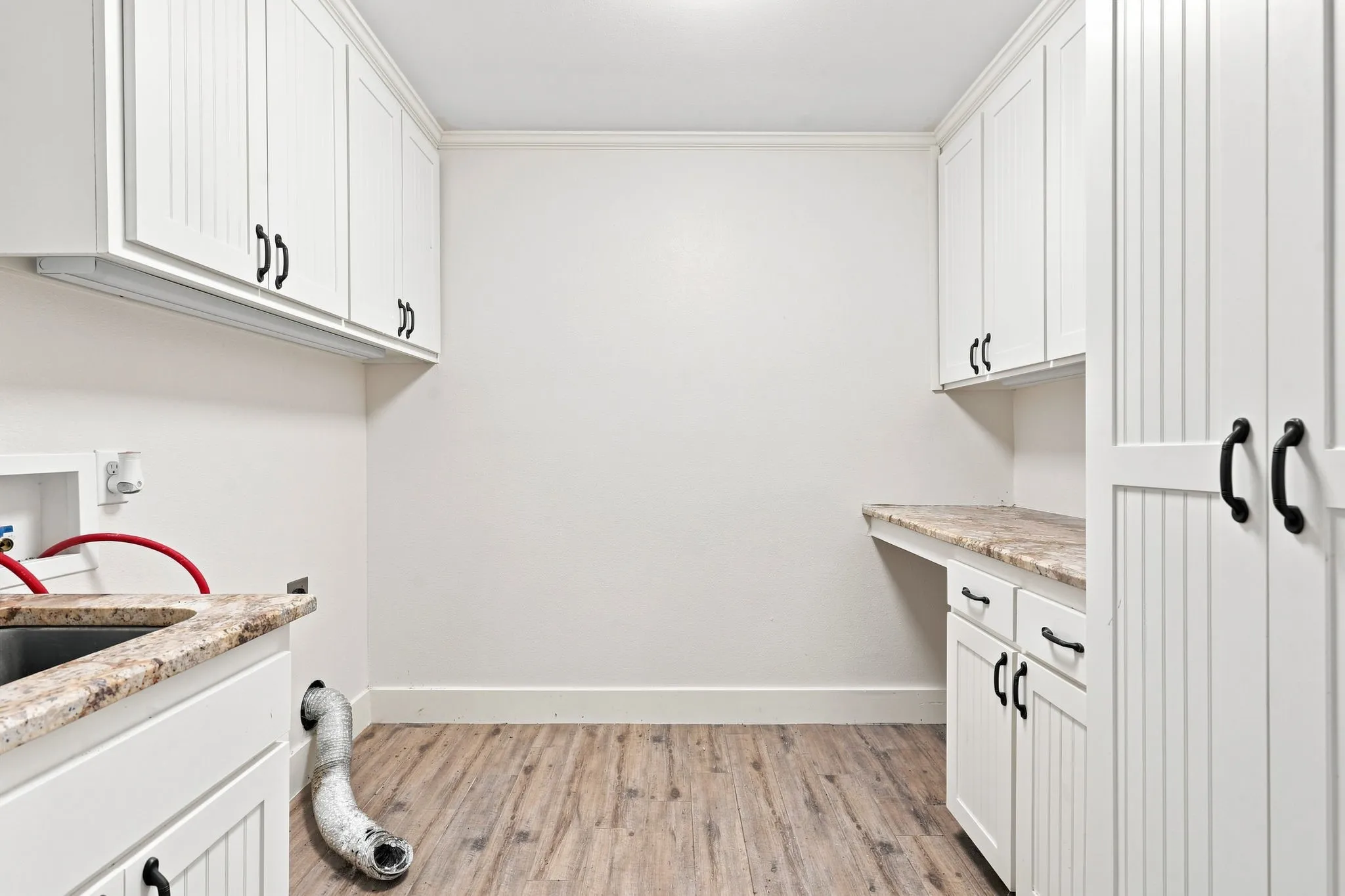 White shaker cabinetry with black hardware, wood-finish flooring, light-toned countertop, and built-in sink
