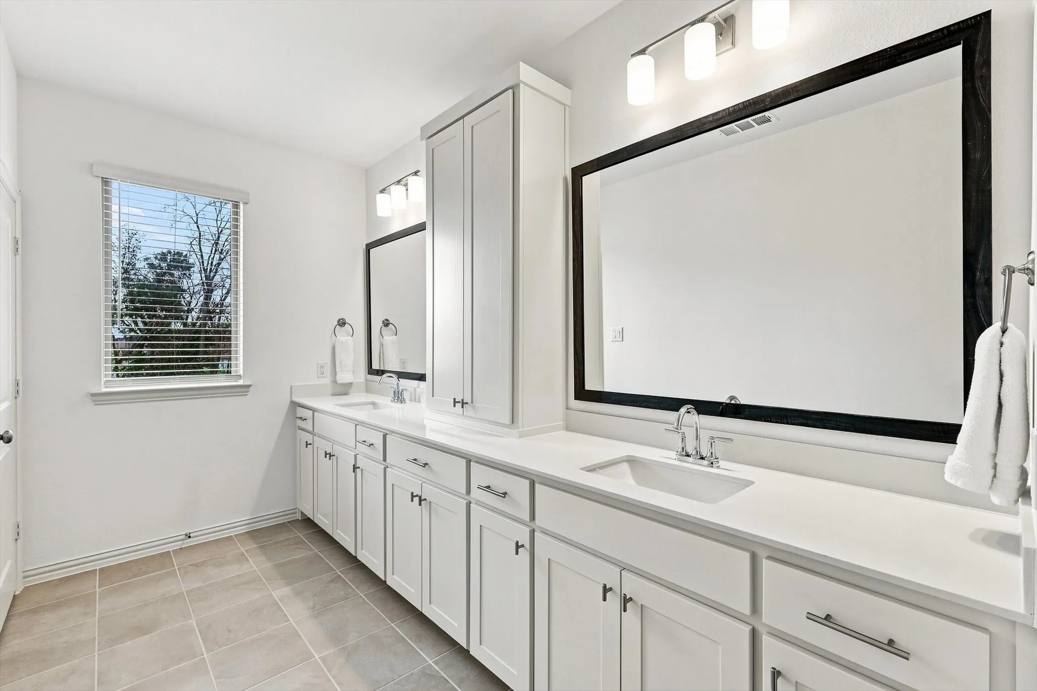 Bright and beautifully appointed, the primary bath offers dual sinks, extensive counter space, generous storage, and natural light.