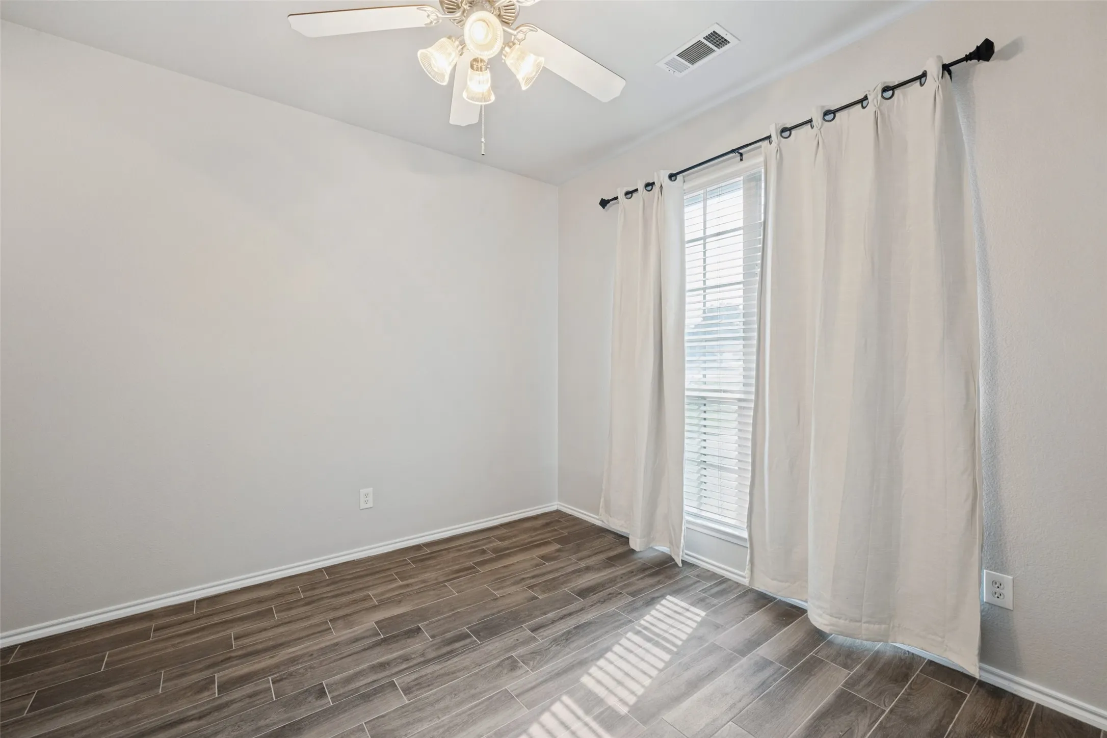 Wood-finish tile flooring, neutral wall tones, window with horizontal blinds, and a ceiling fan with integrated lighting