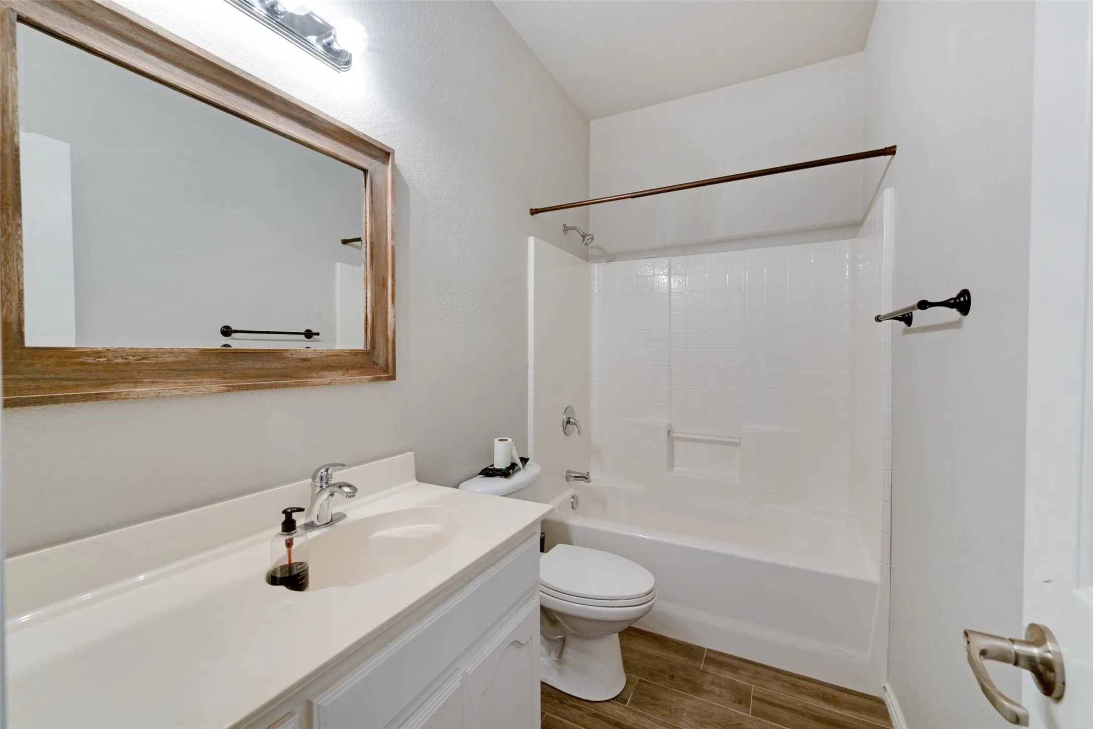 White vanity with integrated sink, wood-finish flooring, and a shower-tub combination
