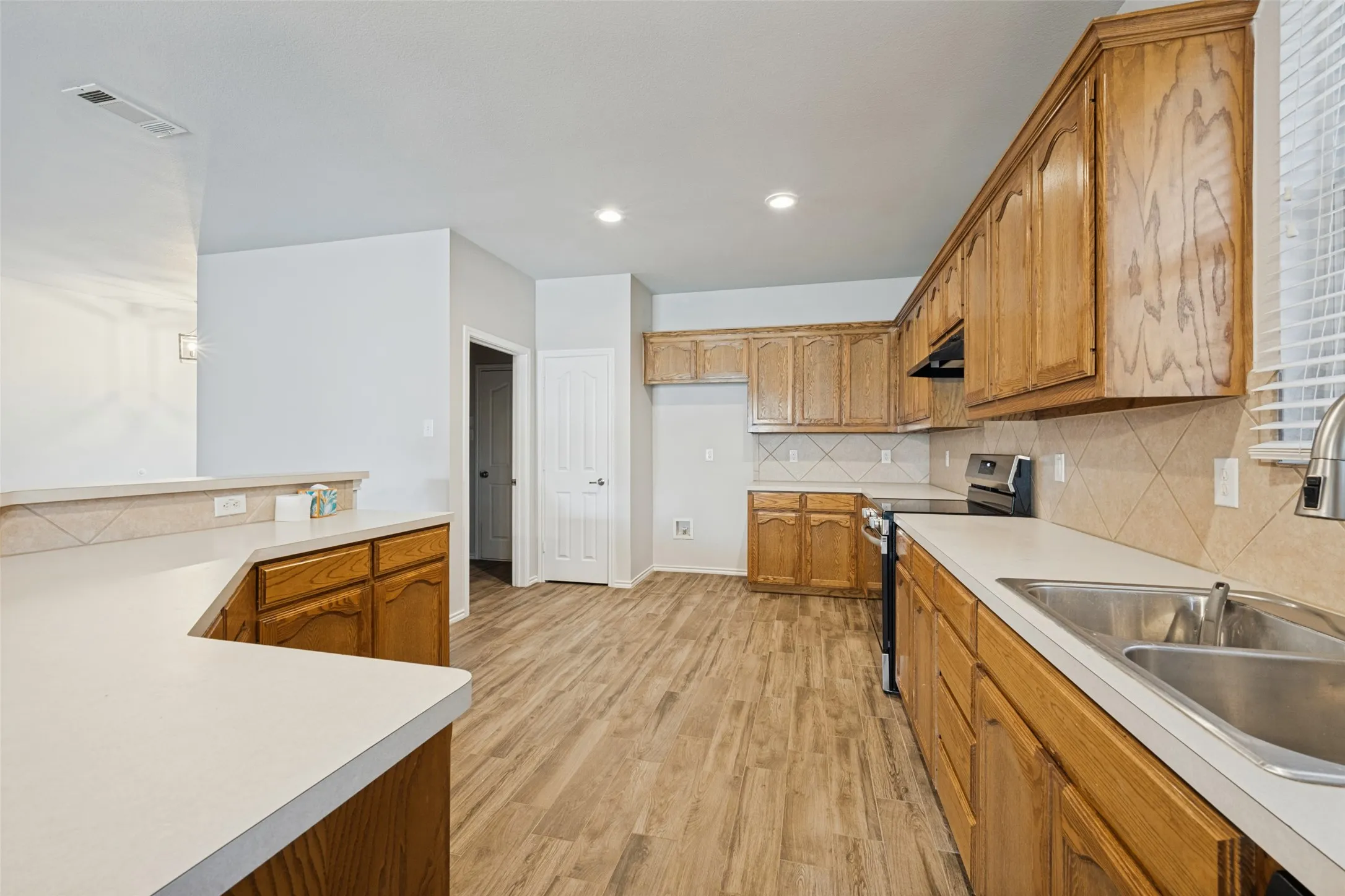 Expansive kitchen featuring wood-finish cabinetry, light-toned countertops, and wood-finish flooring