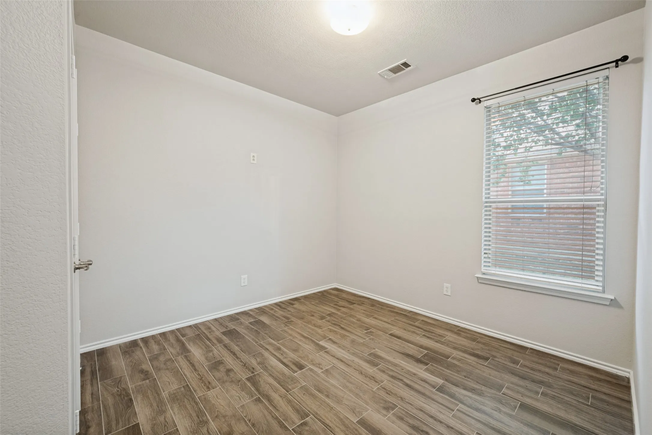 Recessed window with blinds, overhead lighting, wood-finish flooring, and light-toned wall finishes