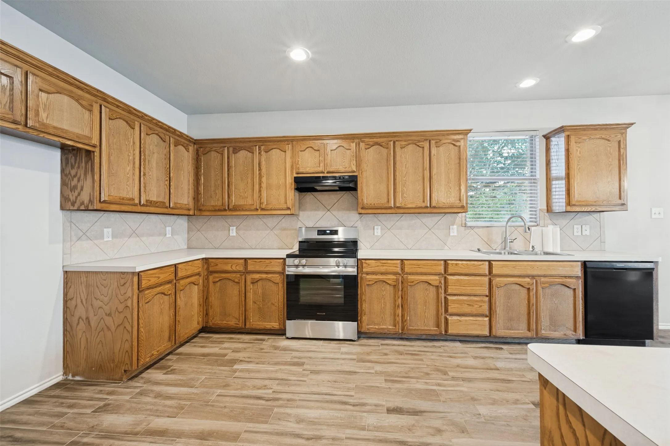 Kitchen with wood-finish cabinetry, solid surface countertops, diagonal tile backsplash, stainless steel range, and wood-look flooring
