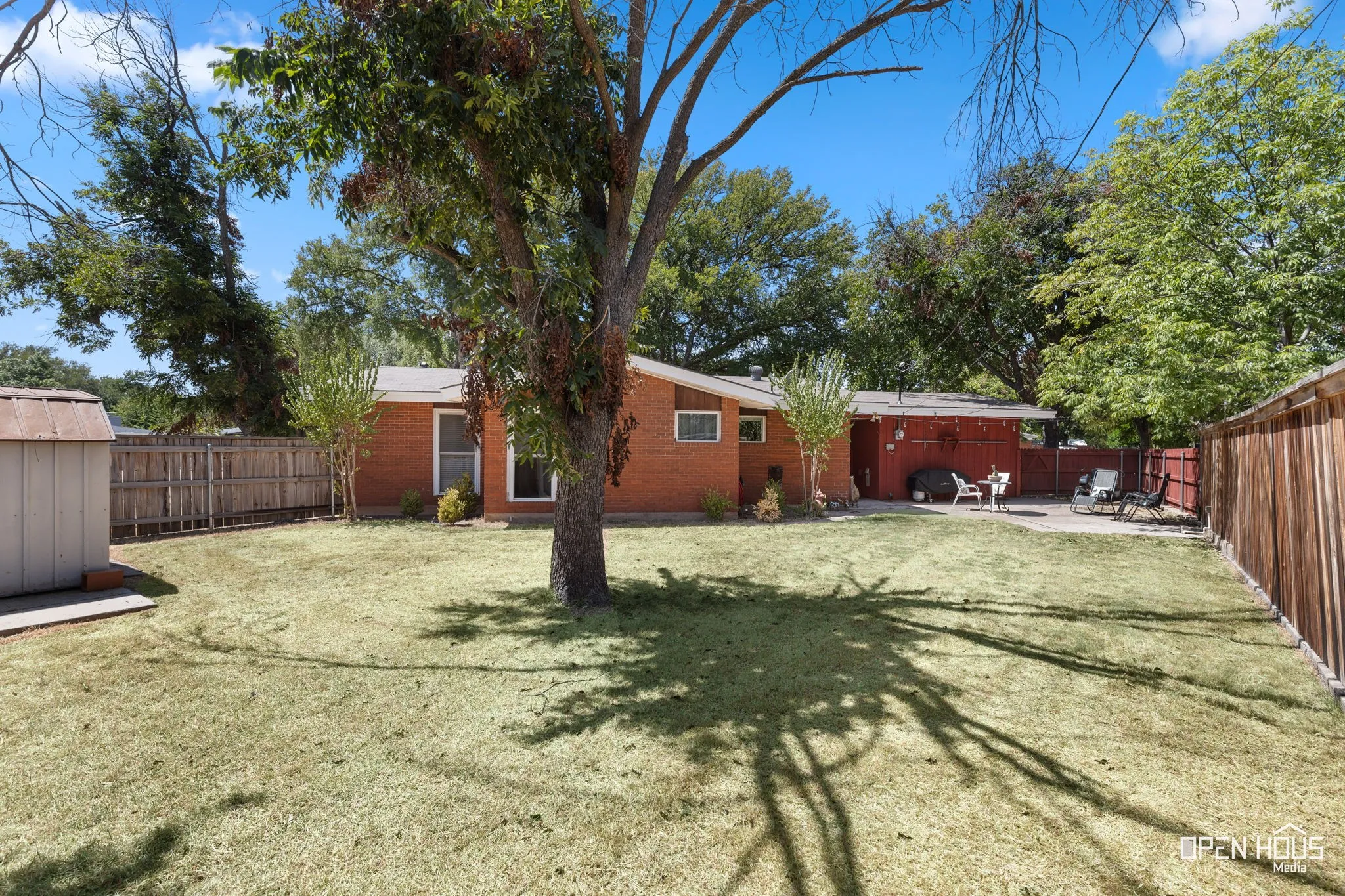 Expansive grassy yard with a privacy fence, mature trees, and a concrete patio