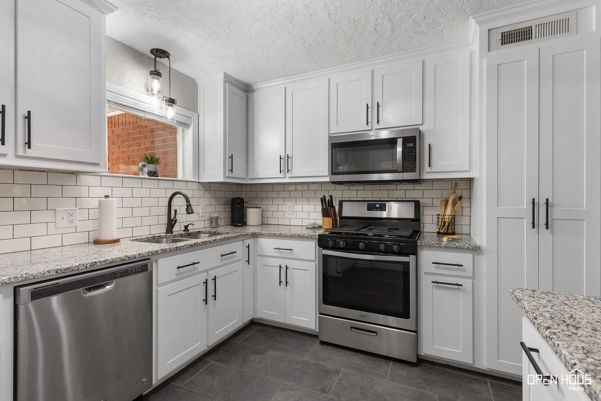 White shaker cabinetry, stainless steel appliances, speckled countertops, subway tile backsplash, and dark tile flooring