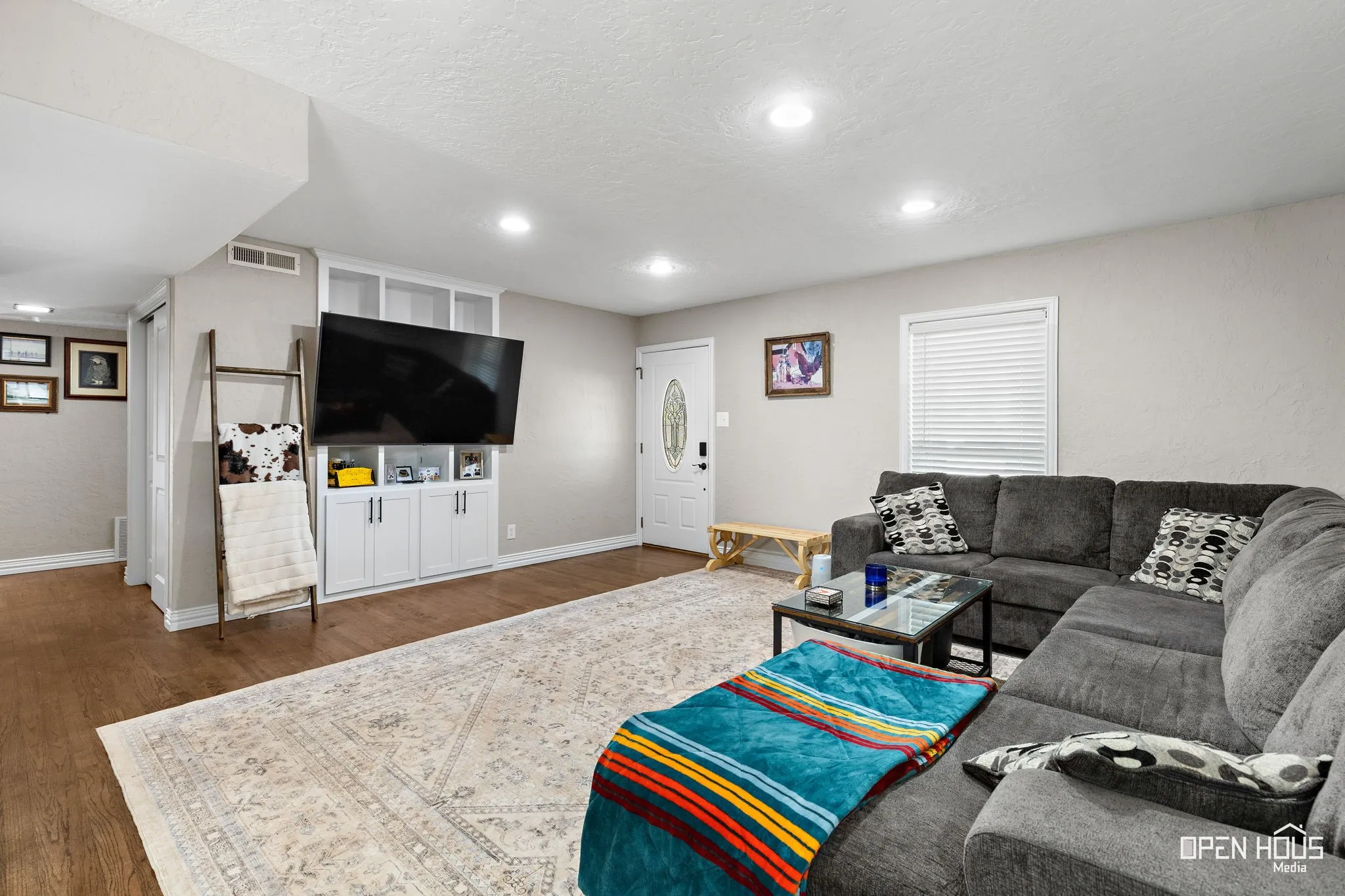 Recessed lighting, wood-finish flooring, built-in media cabinetry, and a white paneled entry door