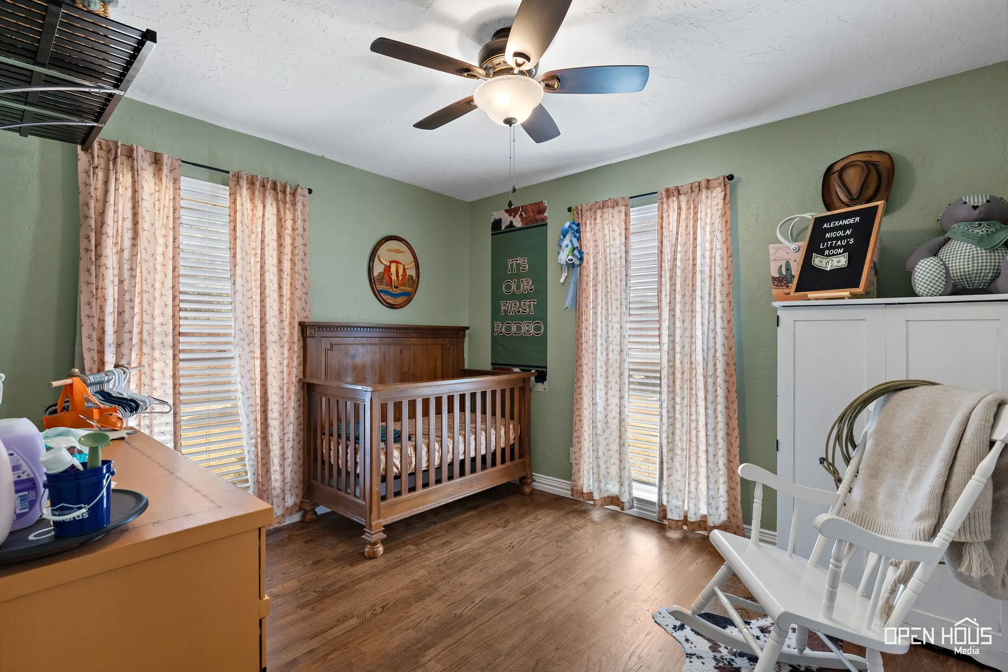 Wood-finish flooring, ceiling fan with light fixture, and two window openings with vertical blinds