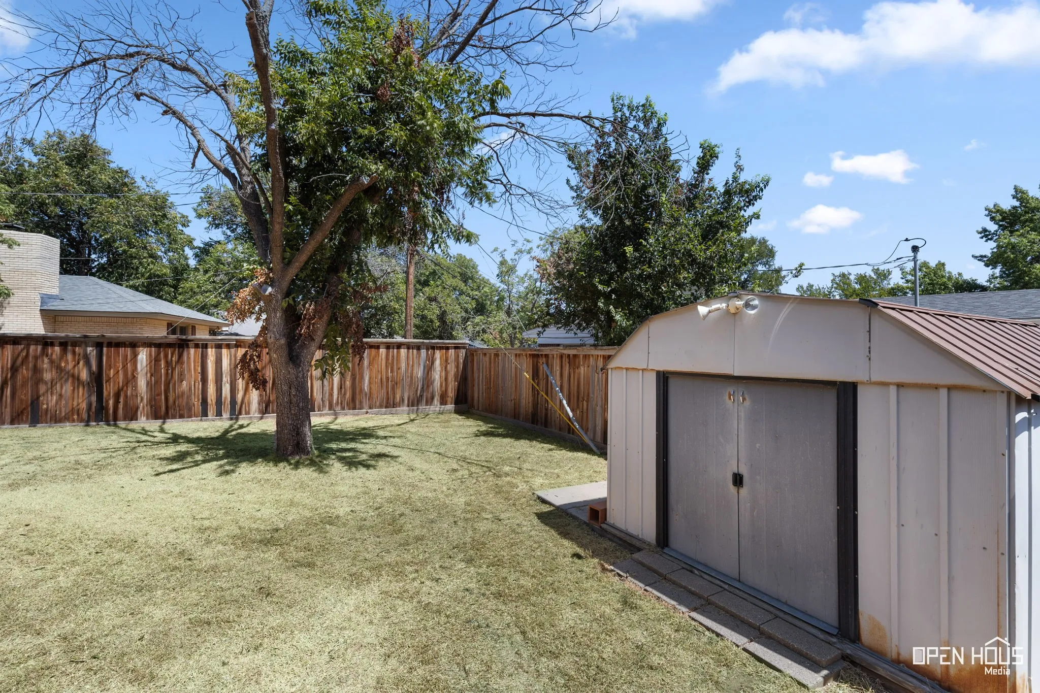 Expansive yard featuring a privacy fence, mature trees, and a storage shed
